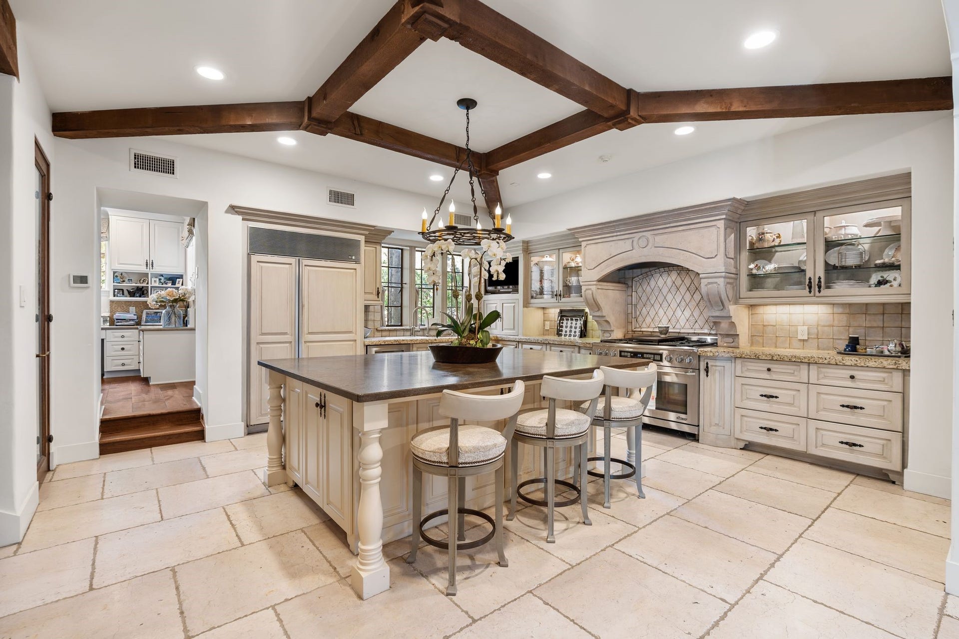 [Kitchen]
The reconfigured and expanded kitchen is Robert Dame's and Slovack-Bass's redesign. Details include a honed stone floor; refectory-style island with dining ledge, storage, microwave, and pull-out trash bin. Note cabinet-front SubZero refrigerator/freezer, Dacor gas range with six burners, and illuminated glass jumper cabinets. Office is visible at right/rear.