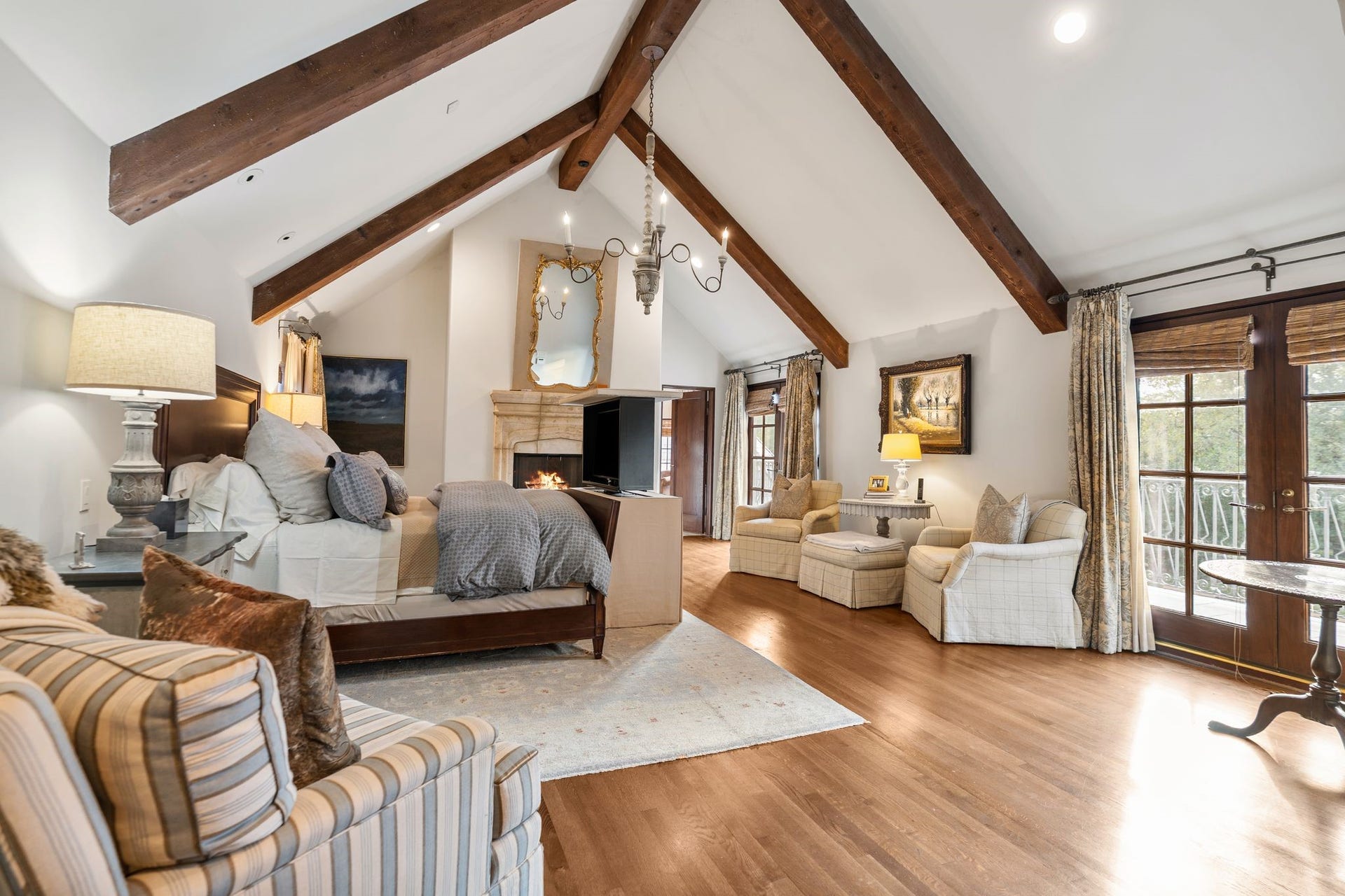 [Primary Bedroom]
The expanded primary bedroom features an exposed-beamed cathedral ceiling, French doors to the balcony over the pool, and a fireplace with marble Tudor arch mantel.