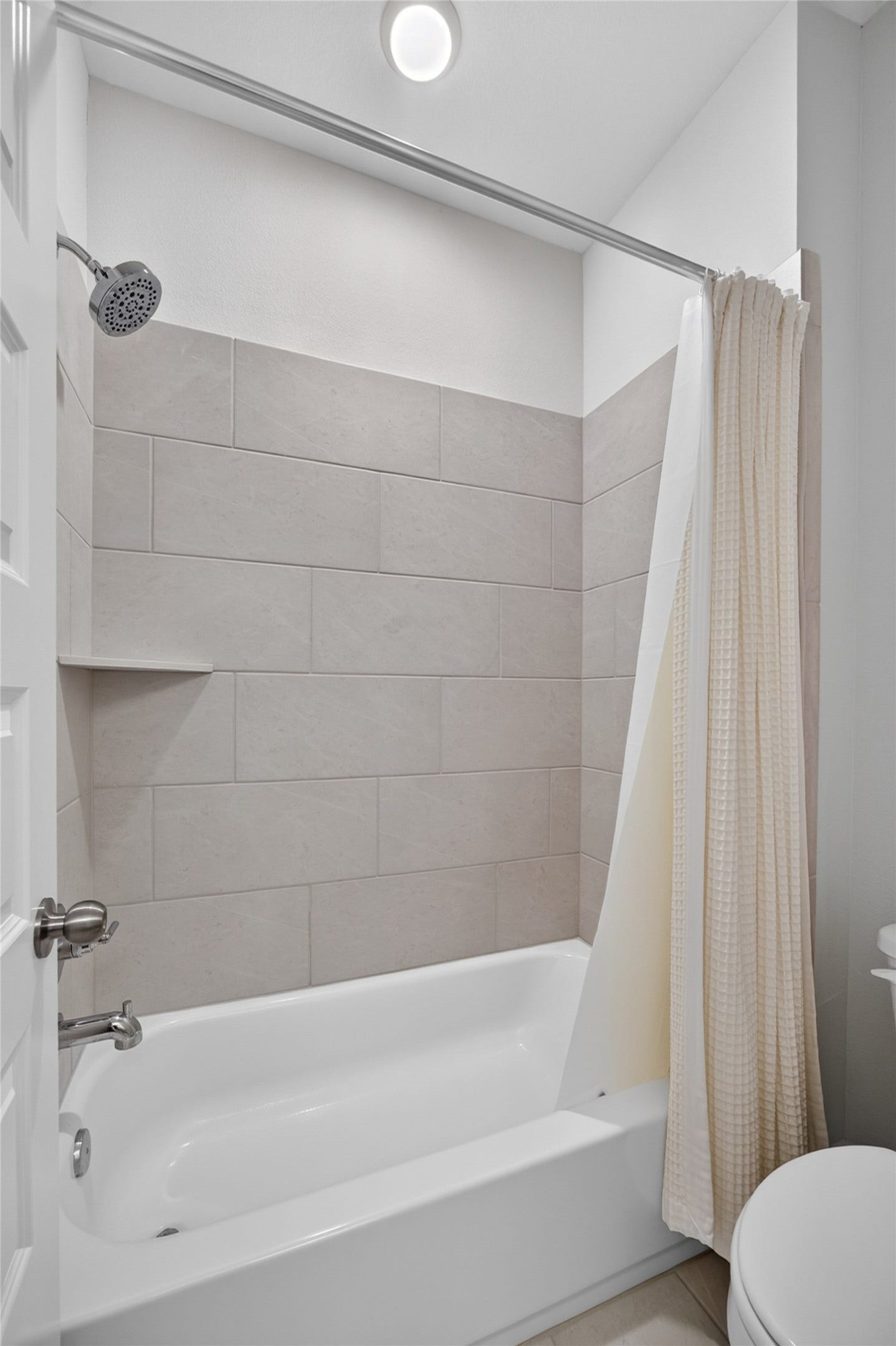 7311 Winding Aster Way, Katy, TX 77493 The secondary bathing area features a tub-and-shower combination with a large-format tile surround. A recessed niche keeps bathing essentials within reach, while the shower curtain allows the tub area to be easily enclosed. Neutral tile offers a versatile backdrop for a variety of decorative accents.