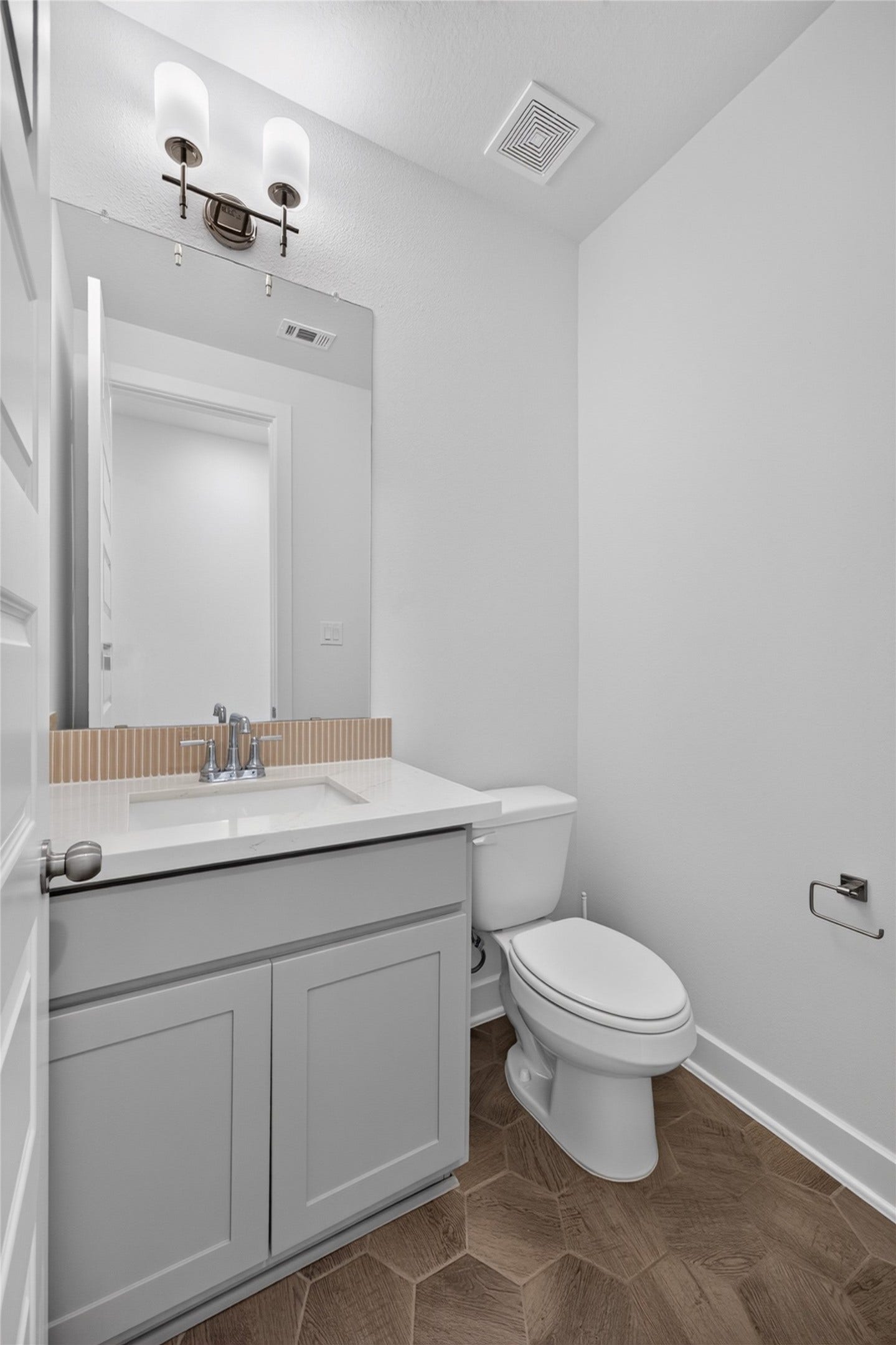 7311 Winding Aster Way, Katy, TX 77493 The first-floor powder room offers a convenient option for guests near the main living areas. A gray vanity pairs with a light countertop and chrome fixtures, while the large mirror enhances the sense of space. Cabinet storage keeps everyday essentials neatly tucked away.