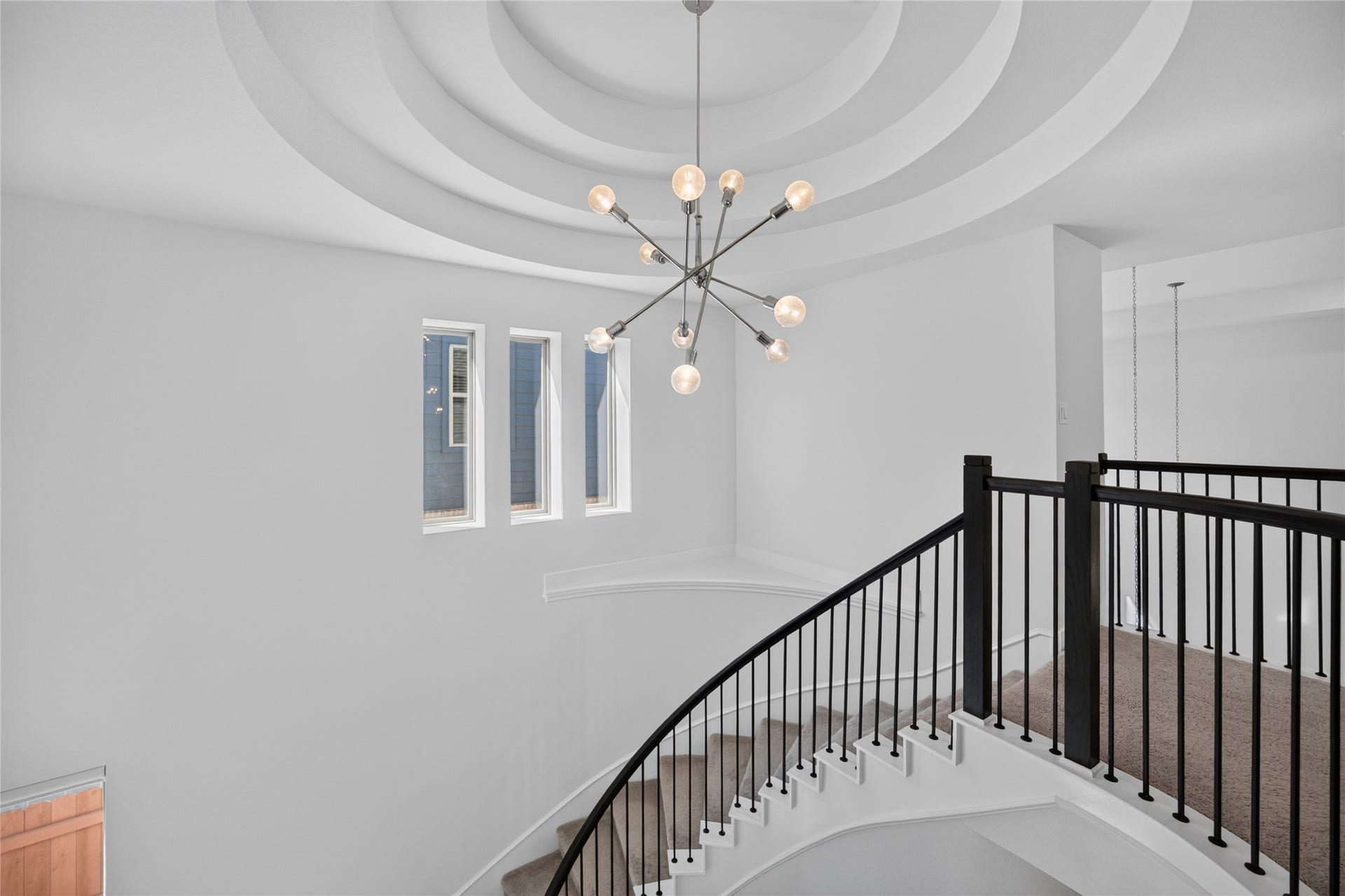 7311 Winding Aster Way, Katy, TX 77493 The upstairs landing provides a close view of the homes dramatic tiered ceiling and contemporary chandelier. Curved iron railing follows the staircase and overlooks the foyer below. A trio of windows introduces natural light and emphasizes the architectural detail of this central space.