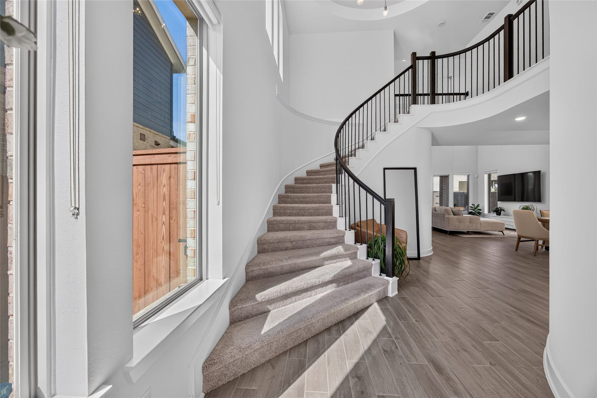 7311 Winding Aster Way, Katy, TX 77493 The foyer makes a memorable entrance with a sweeping curved staircase, dark handrail and iron balusters. Tall windows illuminate the stairway, while the soaring ceiling emphasizes the homes vertical space. Wood flooring continues toward the main living areas, creating visual continuity throughout the first floor.