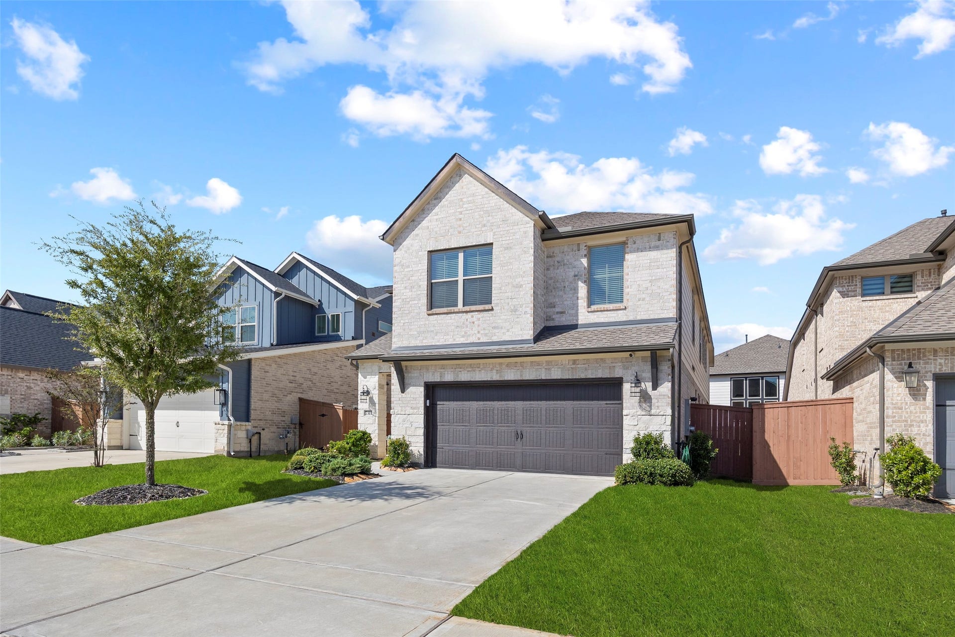 7311 Winding Aster Way, Katy, TX 77493 This angled view highlights the homes architectural lines, light brick exterior and contrasting garage door. A double-width driveway provides access to the attached two-car garage, while the front lawn, planting beds and established tree soften the approach to the covered entry.