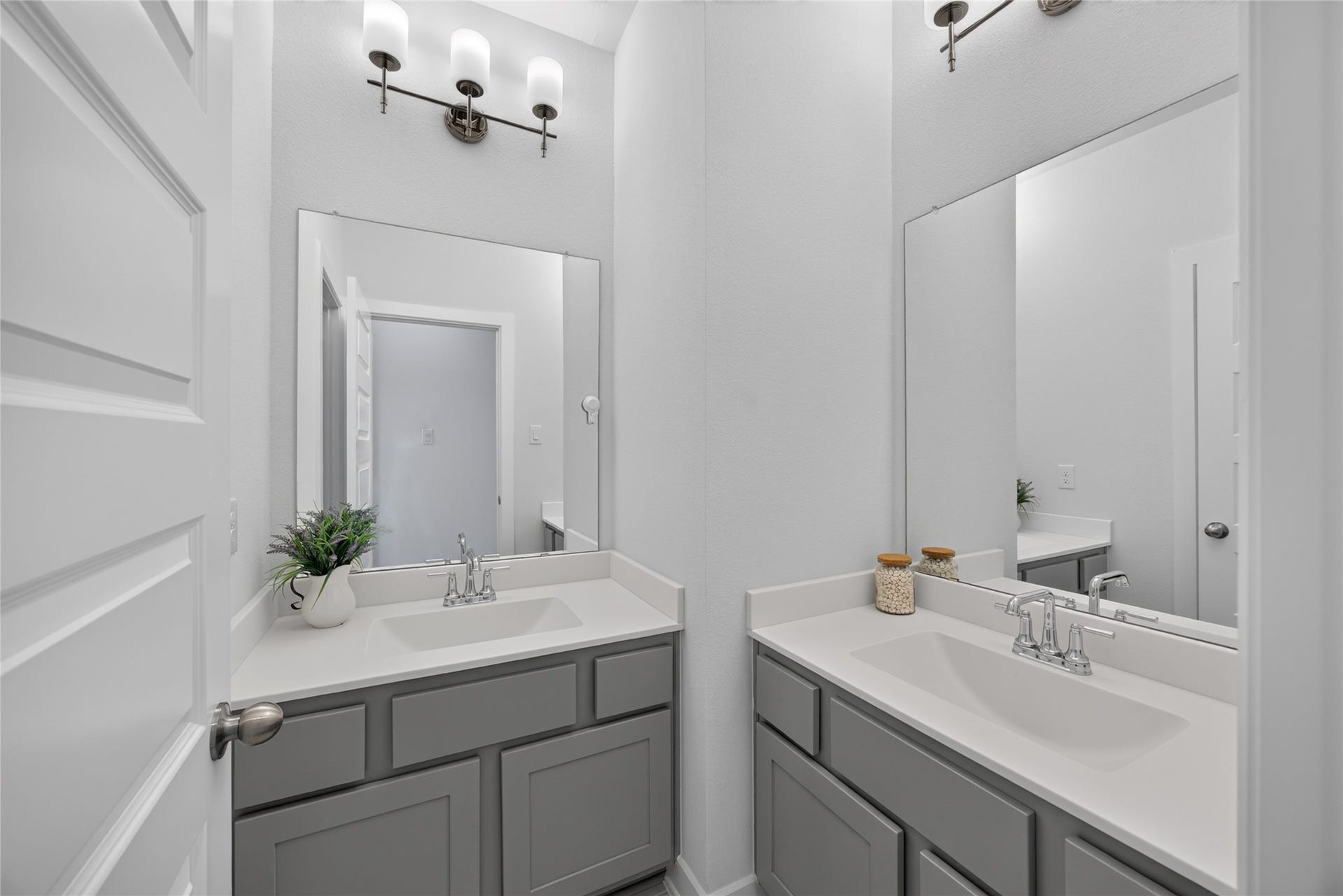 7311 Winding Aster Way, Katy, TX 77493 Two separate vanity areas provide individual sinks, mirrors and cabinet storage in this secondary bathroom. The arrangement creates distinct spaces for daily routines, with light countertops and gray cabinetry maintaining a cohesive appearance. An adjoining doorway connects the vanity space to the bathing area.