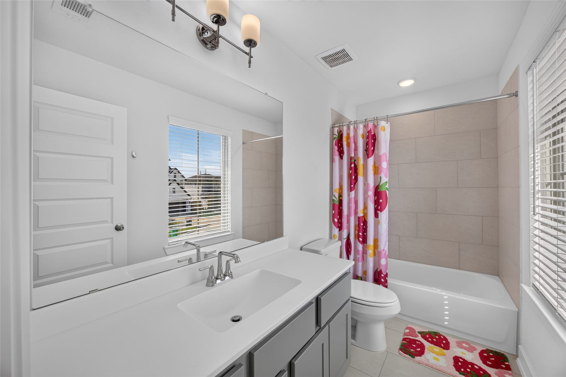 7311 Winding Aster Way, Katy, TX 77493 This secondary bathroom includes a long vanity with cabinet storage, a large mirror and a window for natural light. The tub-and-shower combination features a tiled surround, offering flexibility for daily bathing. Light walls and gray cabinetry coordinate with the finishes used elsewhere in the home.