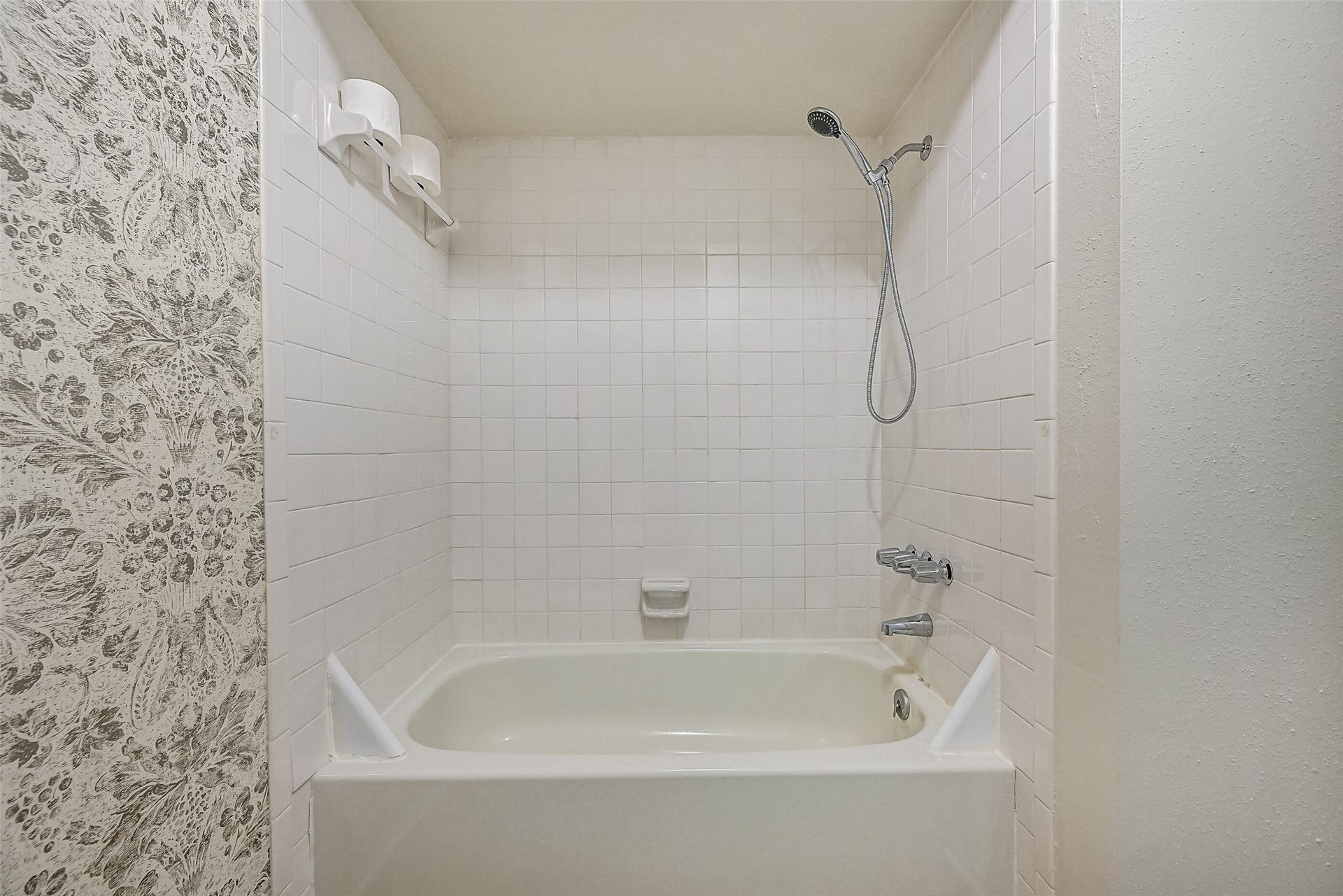 5005 Georgi Lane, #155, Houston, TX 77092 The primary bathroom includes a white tiled tub/shower combination with a handheld showerhead, built-in soap dish & towel bar. The adjoining vanity features a granite countertop & white cabinetry, while the separate bathing area offers a practical layout with everything within easy reach.