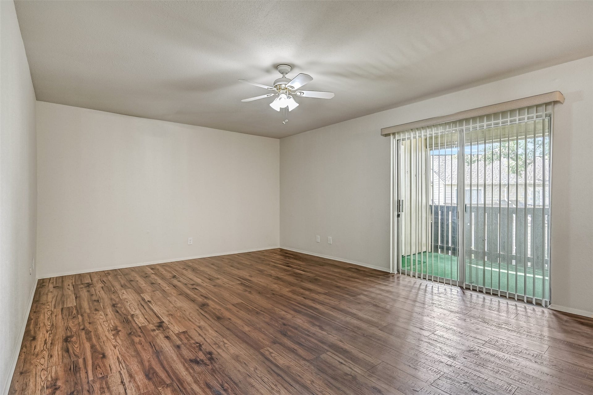5005 Georgi Lane, #155, Houston, TX 77092 Another view of the spacious living room highlights the sliding glass doors opening to the oversized covered balcony. Wood-look flooring extends throughout the room, while a ceiling fan with lighting adds comfort. The generous wall space allows for a variety of furniture arrangements.