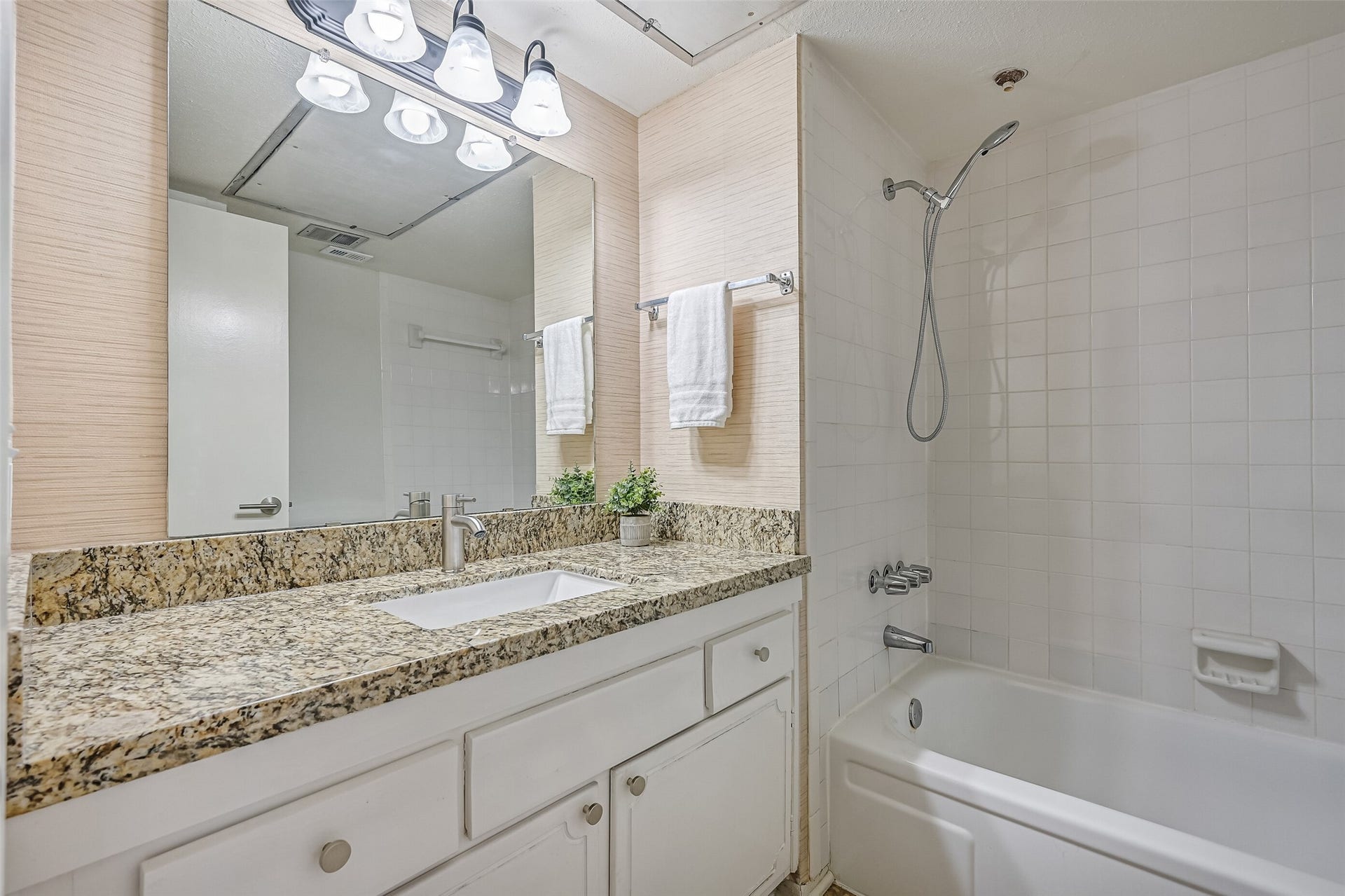 5005 Georgi Lane, #155, Houston, TX 77092 The adjoining full bathroom features a granite countertop with matching backsplash, undermount sink, updated faucet & contemporary vanity lighting. A large wall mirror adds to the open feel, while the white tiled tub/shower combination includes a handheld showerhead for added functionality.