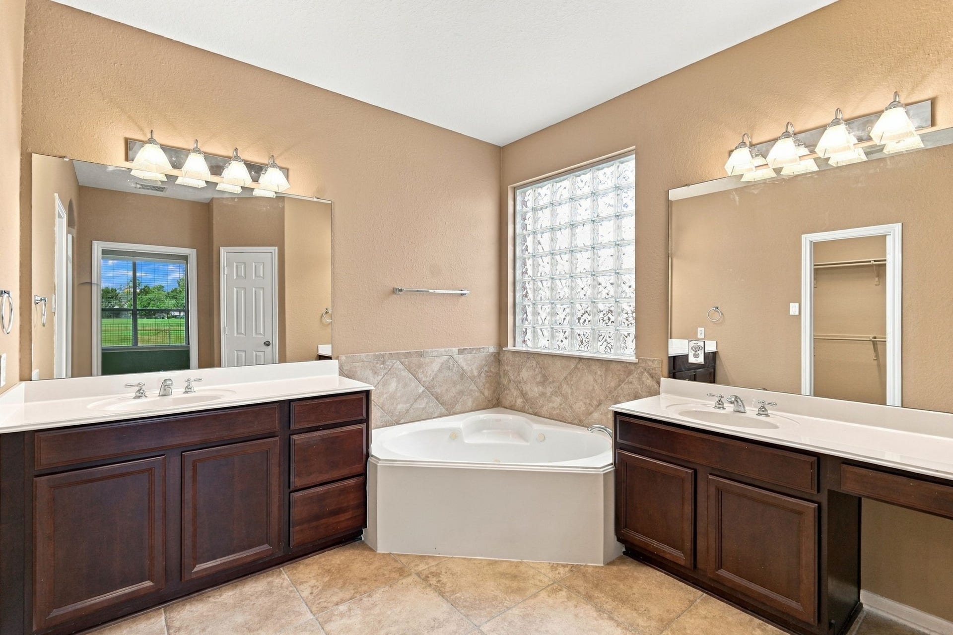 14226 Marin Drive, Cypress, TX 77429 This spacious primary ensuite bath features dual separate vanities with rich wood cabinetry and ample counter space. A luxurious corner soaking tub serves as the centerpiece, flanked by a privacy glass block window.
