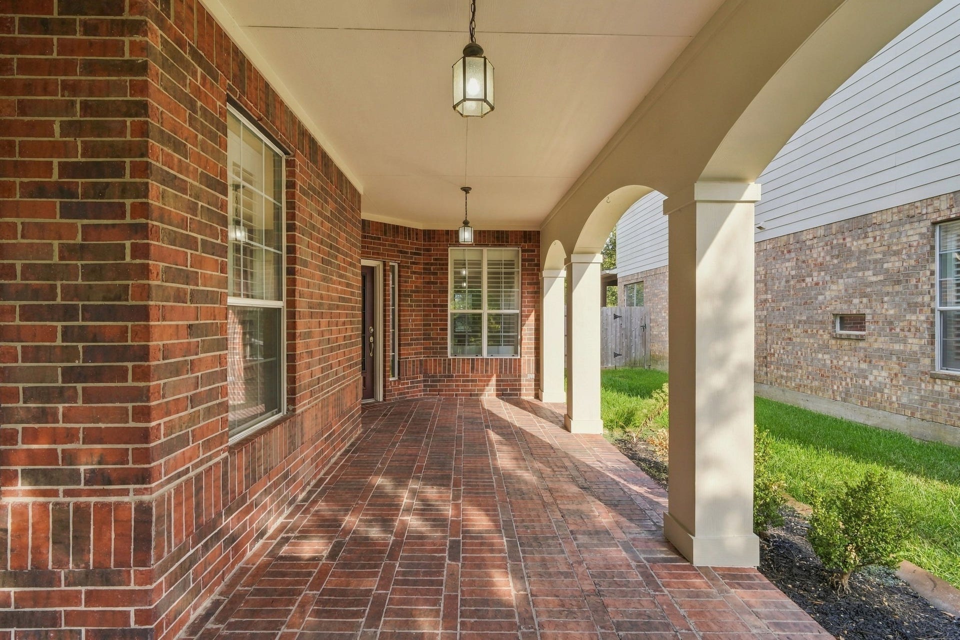 14226 Marin Drive, Cypress, TX 77429 Step into relaxation on this expansive covered porch featuring graceful architectural arches and classic brick flooring. Beautiful pendant lanterns illuminate the pathway, creating a warm retreat.