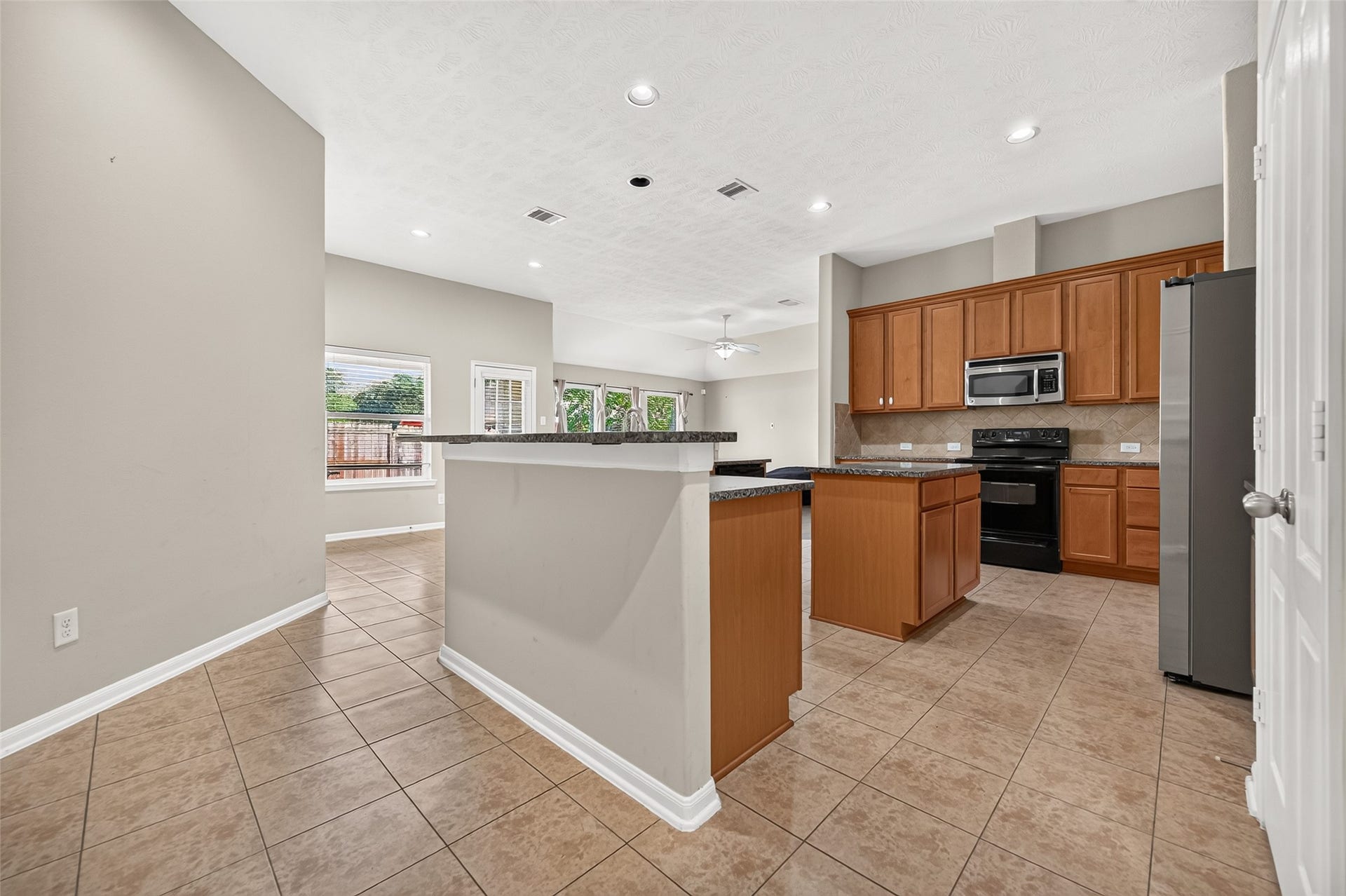 9307 Russeff Field Lane, Rosenberg, TX 77469 Kitchen featuring a center island, warm wood cabinetry, tile flooring, and an open view into the living area.