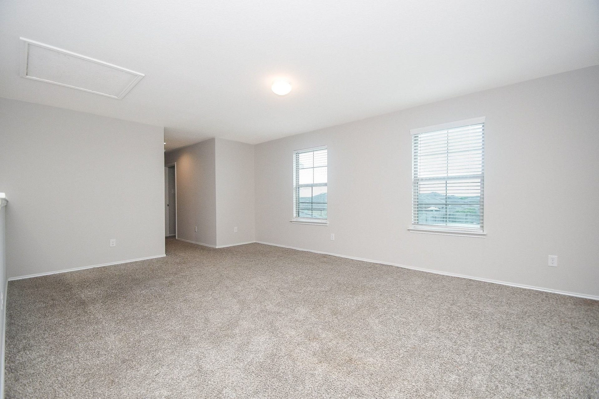 Spacious, carpeted Gameroom upstairs with neutral walls, ample natural light from two windows, and a cozy, inviting atmosphere.