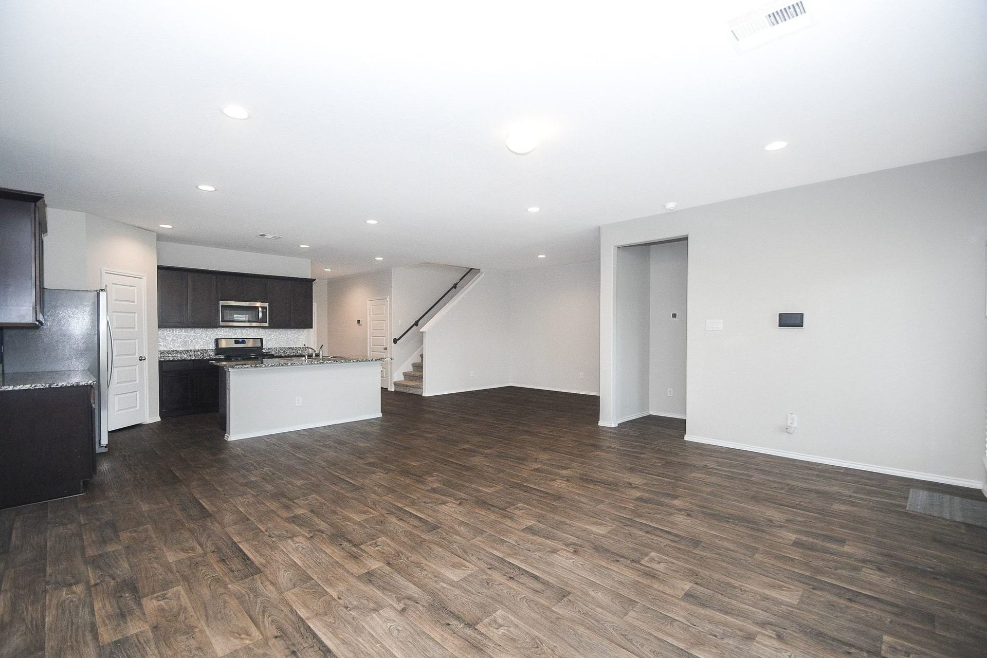 Spacious open-concept living area with sleek hardwood floors, modern kitchen featuring granite countertops and stainless steel appliances, and a convenient staircase leading to the upper level.