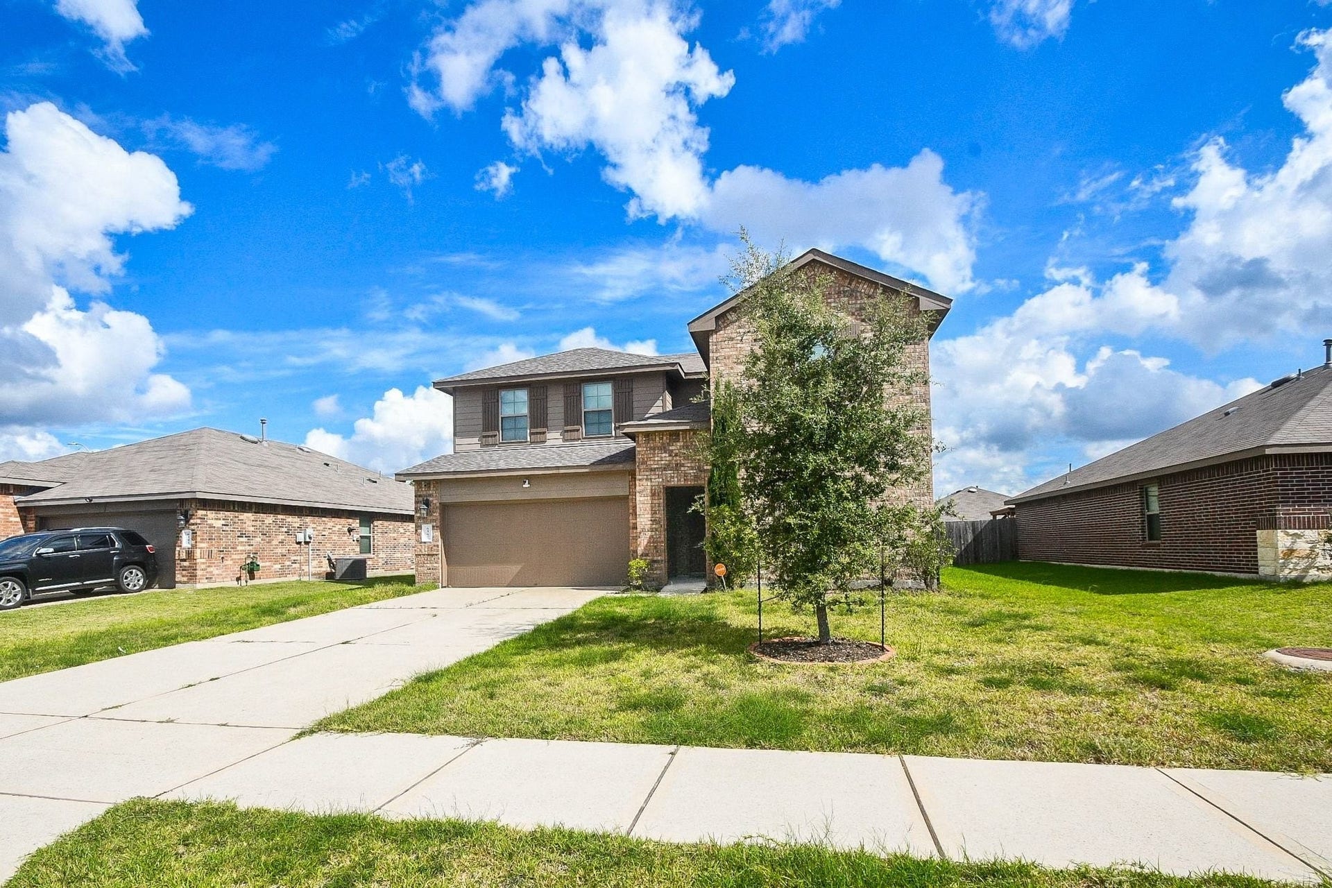 Another view of the charming two-story brick home with a spacious driveway and manicured lawn, set against a backdrop of a clear blue sky.