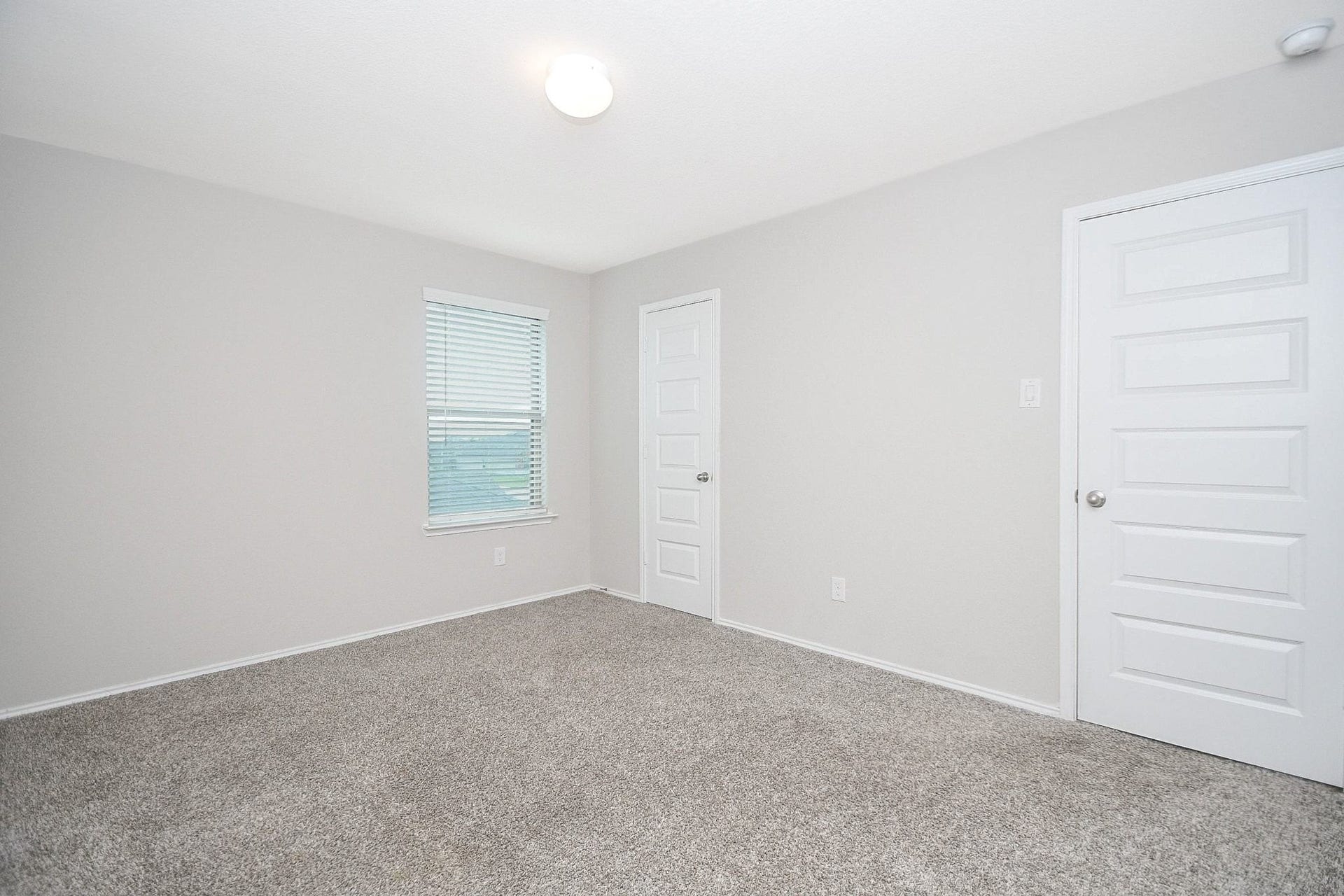 Bright and spacious fourth bedroom upstairs with neutral walls, plush carpeting, and ample natural light from a large window.