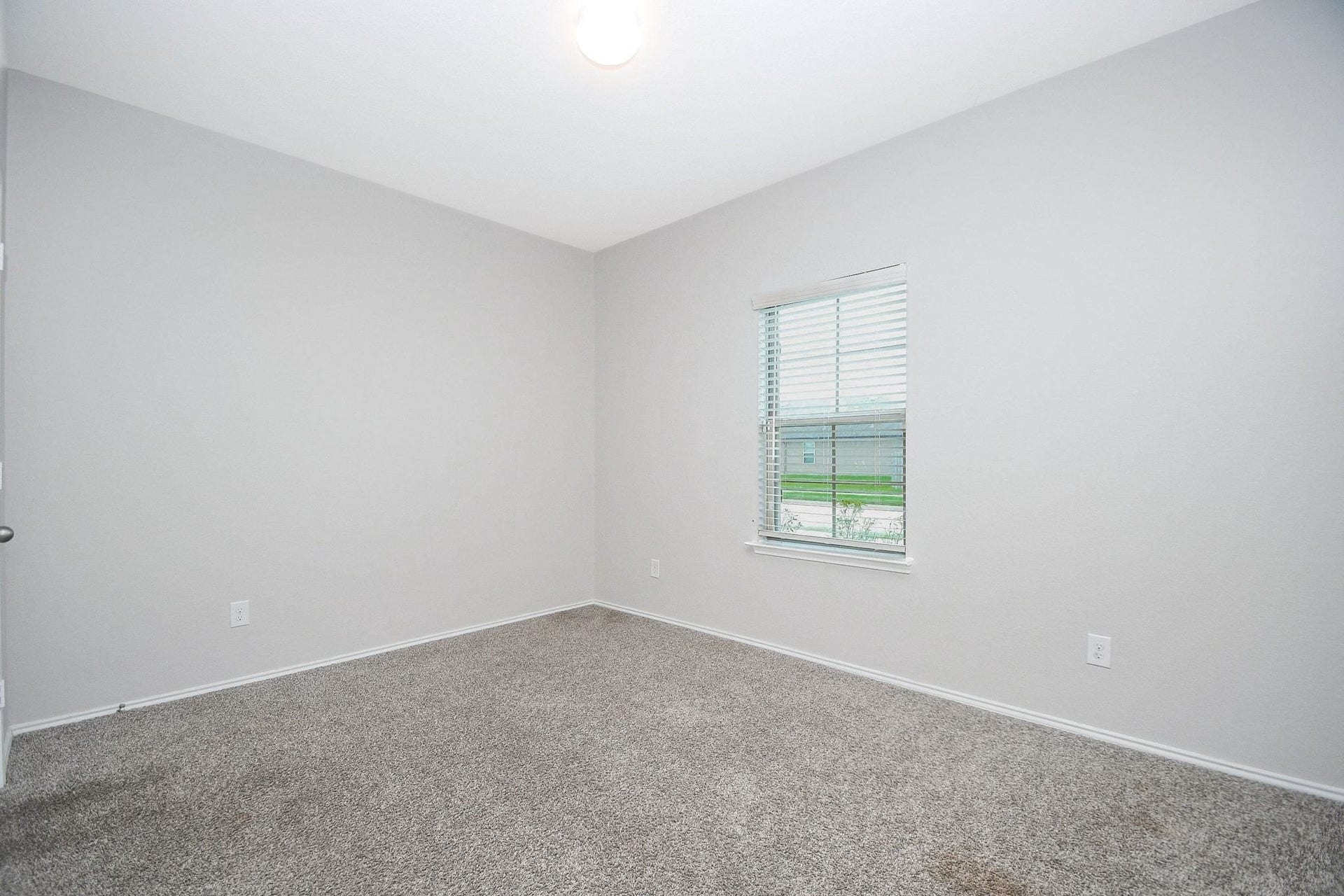 Bright and inviting secondary bedroom downstairs with soft carpeting, neutral walls, and a window providing ample natural light.