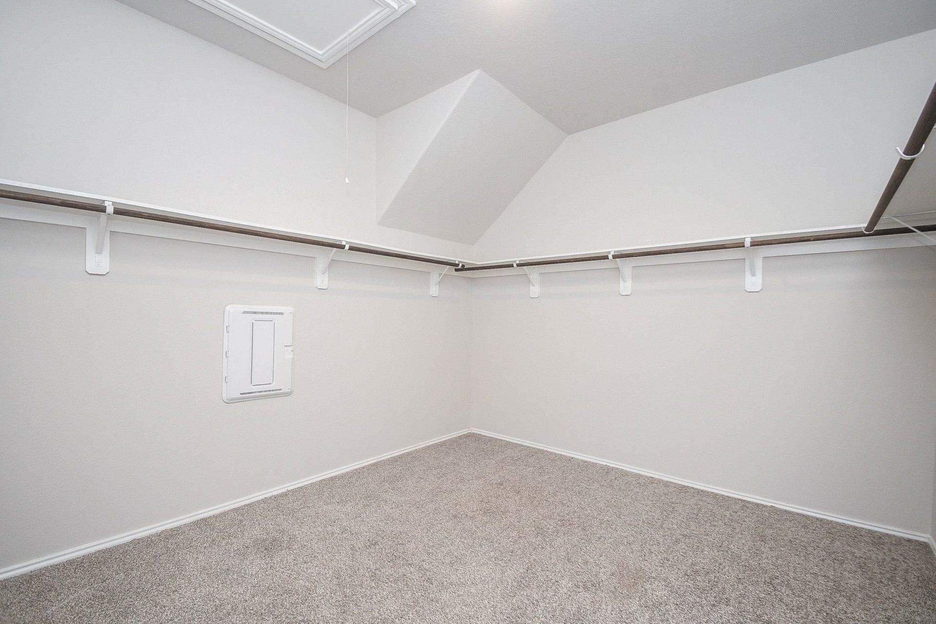 Spacious primary bedroom walk-in closet with ample hanging space and neutral carpeting, perfect for organizing your wardrobe.
