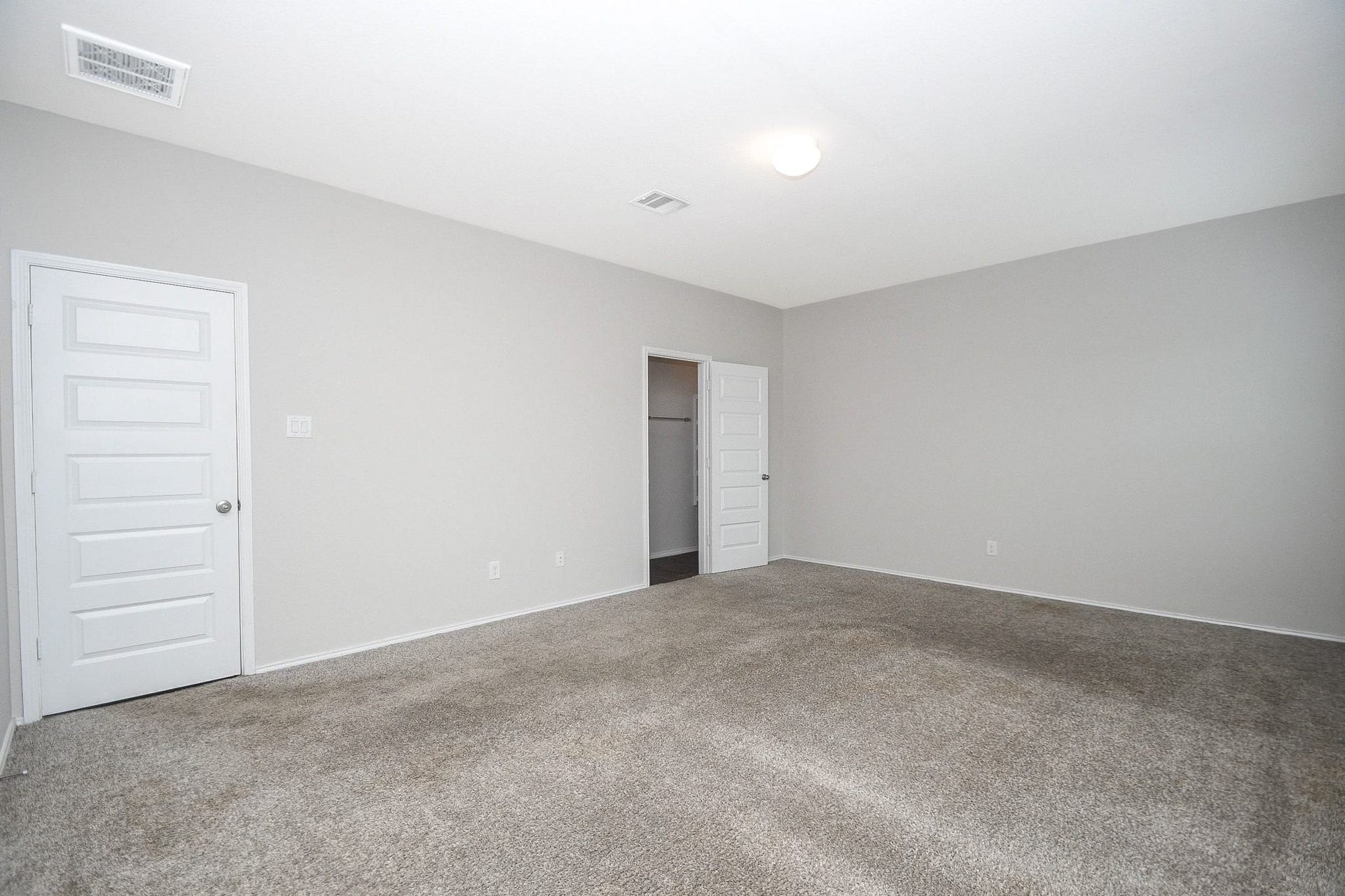 Another view of the spacious primary bedroom with neutral walls, plush carpeting, and ample natural light, featuring closet for convenient storage.