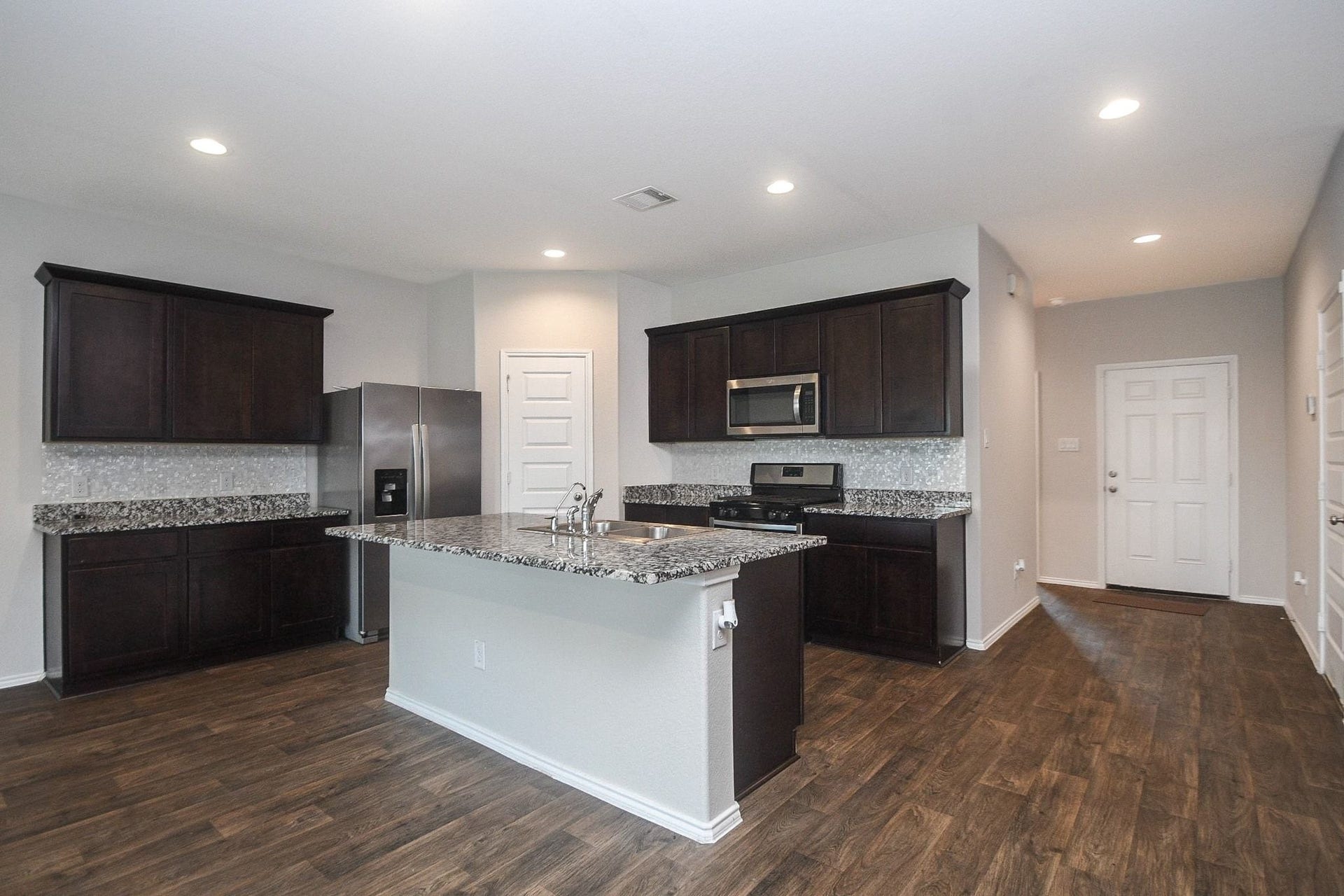 Another view of the modern kitchen with sleek dark cabinetry, granite countertops, and stainless steel appliances, complemented by rich wood flooring and recessed lighting.