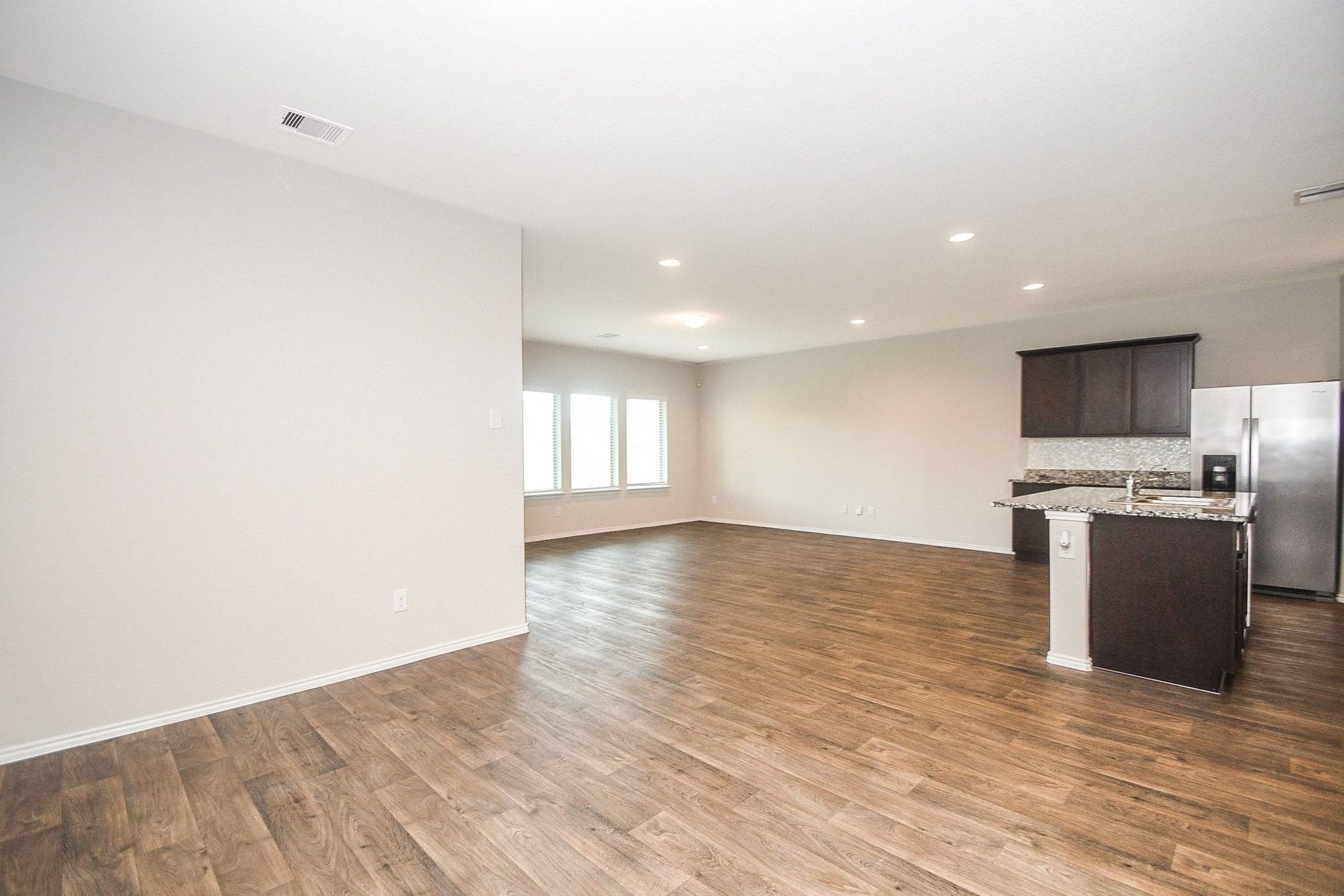 Spacious open-concept living area with rich hardwood flooring, recessed lighting, and a modern kitchen featuring granite countertops and stainless steel appliances.