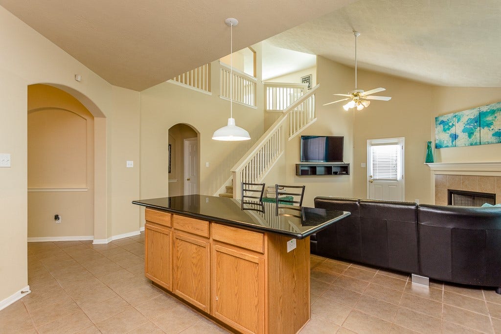 4530 Hall Croft Chase Lane, Katy, TX 77449 Spacious living area with high ceilings, featuring a modern kitchen island, cozy fireplace, and a staircase leading to the upper level.