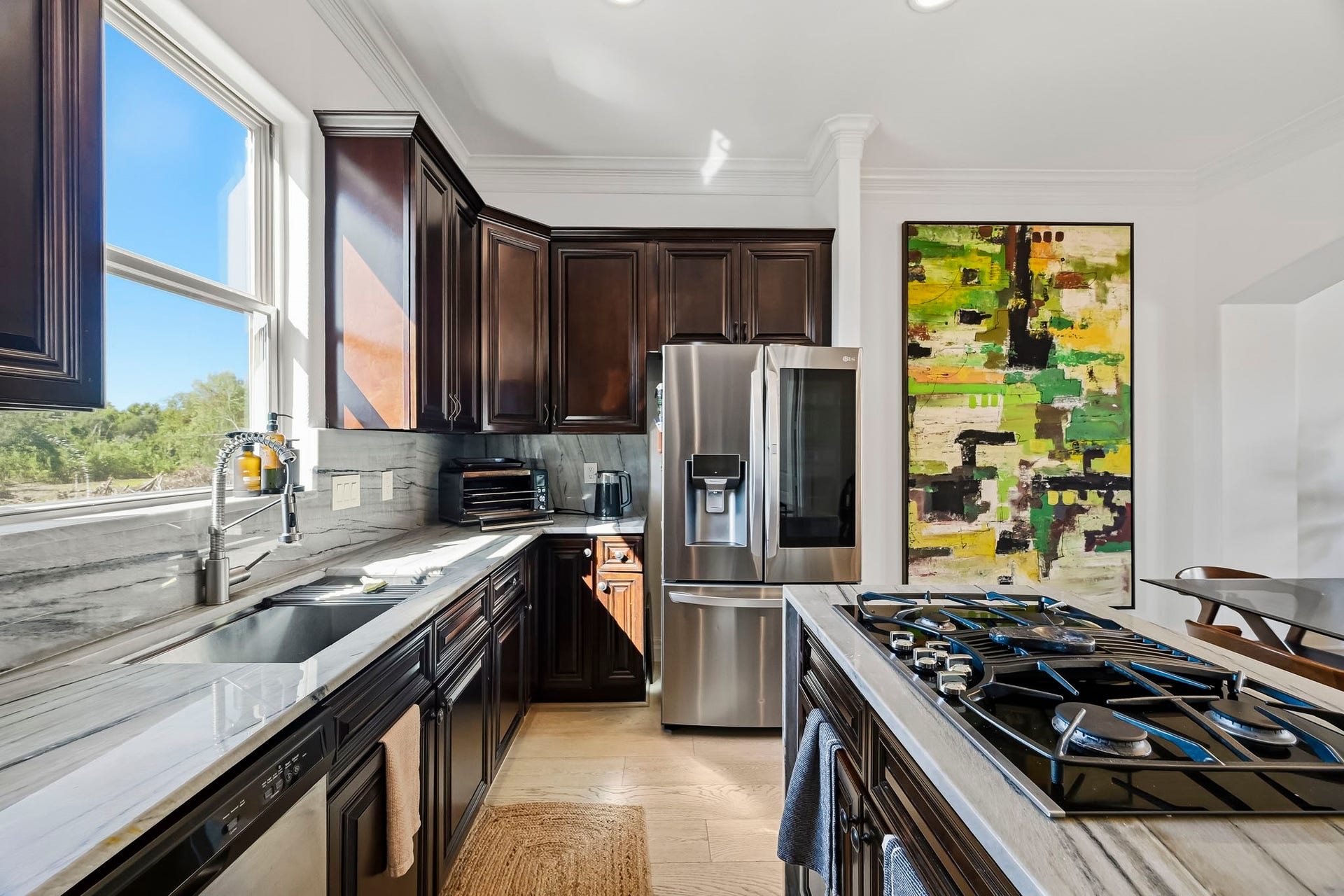 11009 Upland Forest Drive, Houston, TX 77043 Elegant kitchen featuring rich dark wood cabinetry, modern stainless steel appliances, and a stylish gas cooktop, complemented by a large window that brings in abundant natural light.