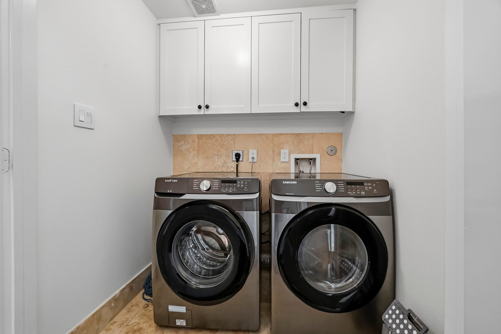 11009 Upland Forest Drive, Houston, TX 77043 Modern laundry area featuring sleek front-loading washer and dryer units, complemented by overhead cabinetry for ample storage.