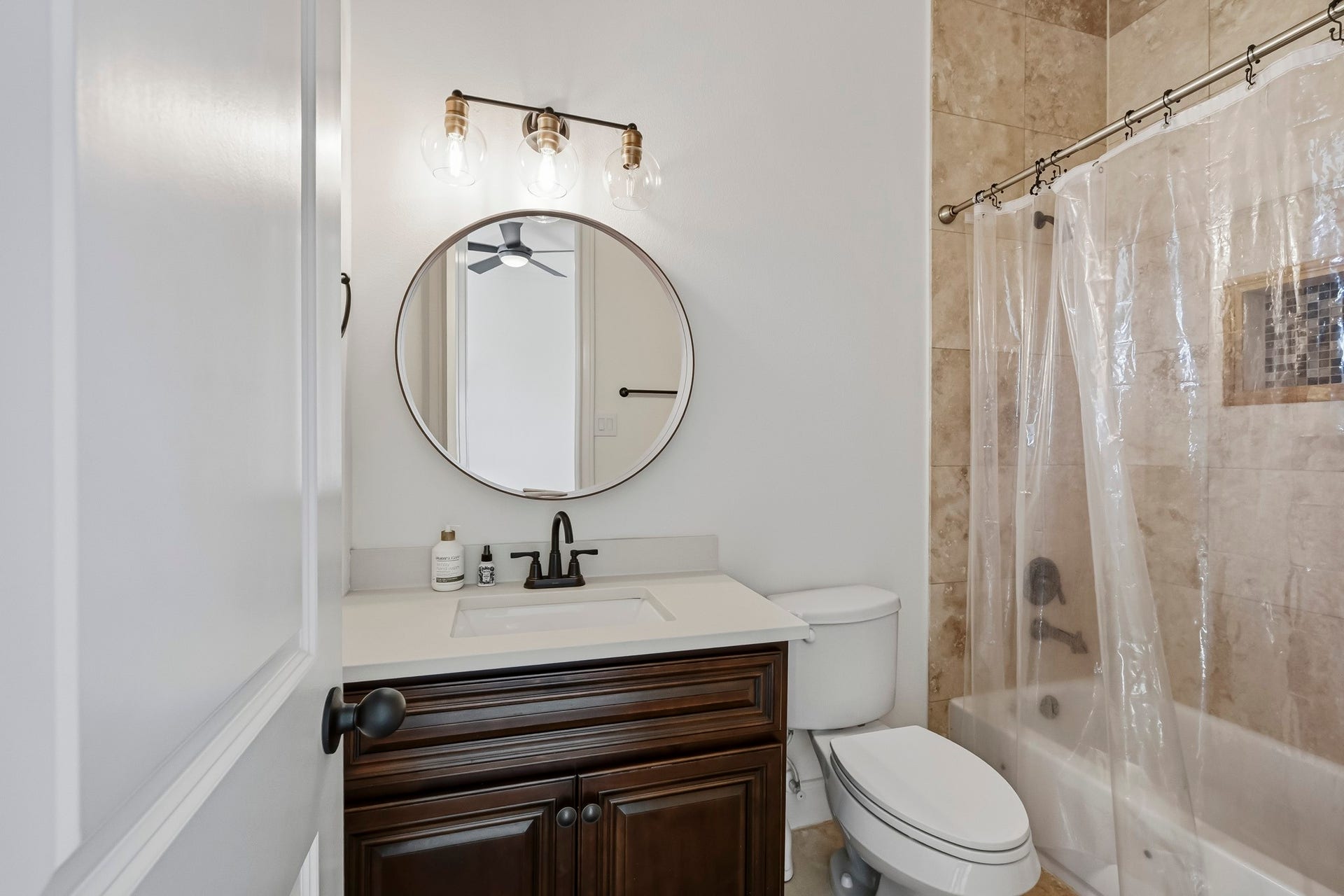 11009 Upland Forest Drive, Houston, TX 77043 Elegant bathroom featuring a modern round mirror, stylish vanity with dark wood cabinetry, and a shower with natural stone tile.