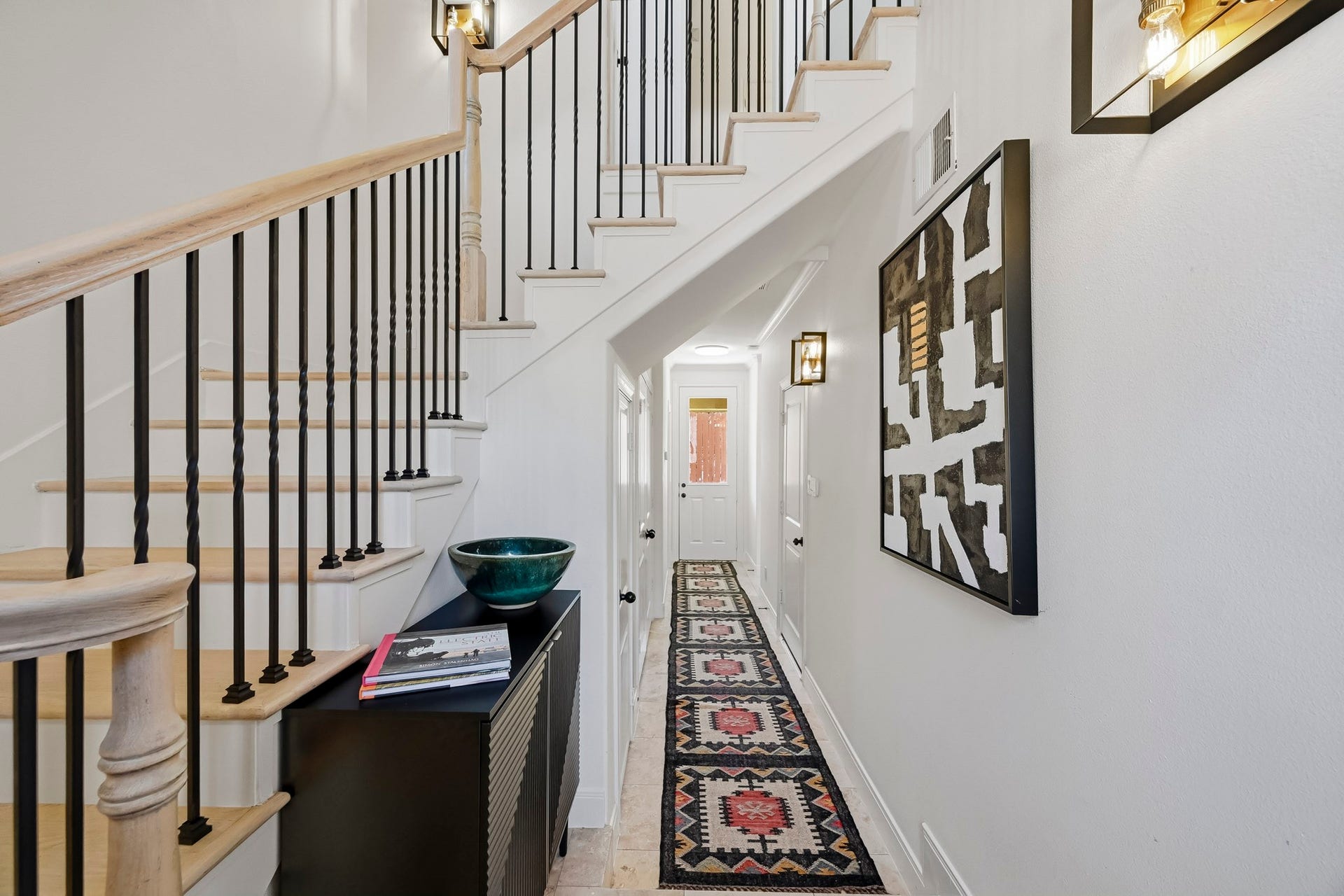 11009 Upland Forest Drive, Houston, TX 77043 Bright and inviting entryway featuring a stylish staircase with wrought iron balusters, modern lighting, and a chic hallway runner leading to a well-lit back door.