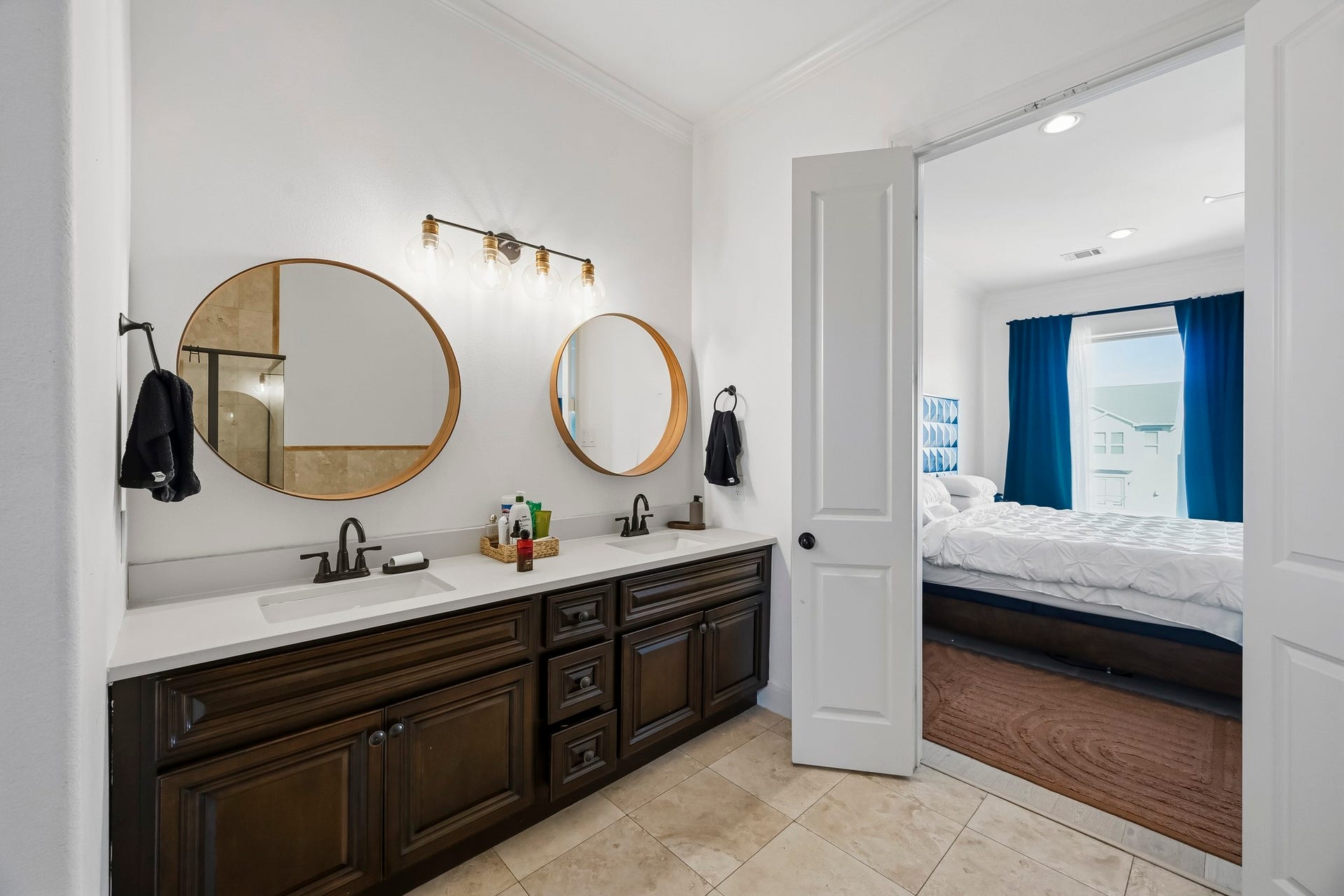 11009 Upland Forest Drive, Houston, TX 77043 Elegant bathroom with dual vanity, stylish round mirrors, and modern fixtures, seamlessly leading into a bright bedroom with a cozy atmosphere.