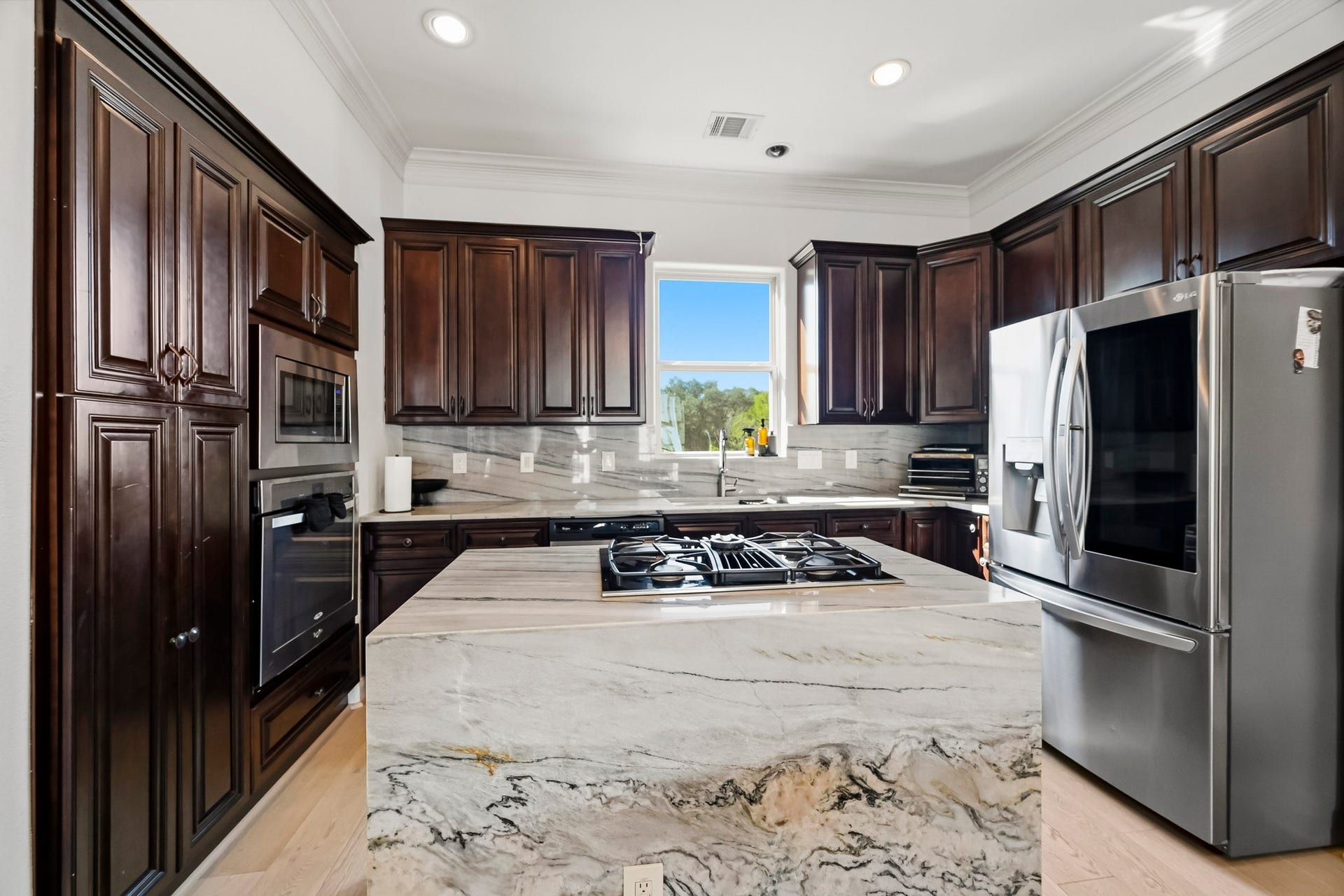 11009 Upland Forest Drive, Houston, TX 77043 Elegant kitchen featuring rich dark wood cabinetry, a sleek marble island with a built-in cooktop, and modern stainless steel appliances.