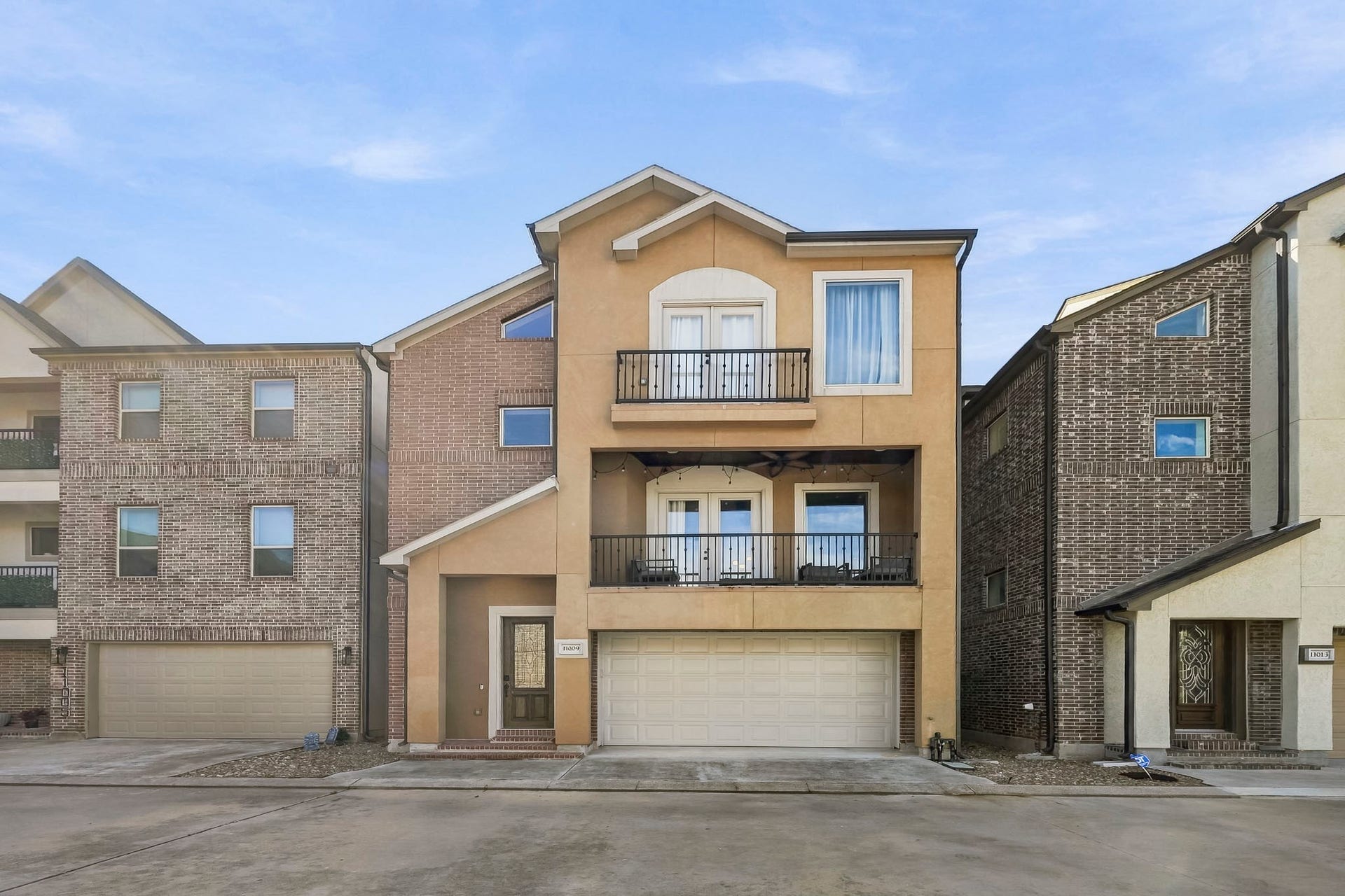 11009 Upland Forest Drive, Houston, TX 77043 Modern three-story townhouse with a warm, inviting facade, featuring two balconies and a spacious two-car garage.