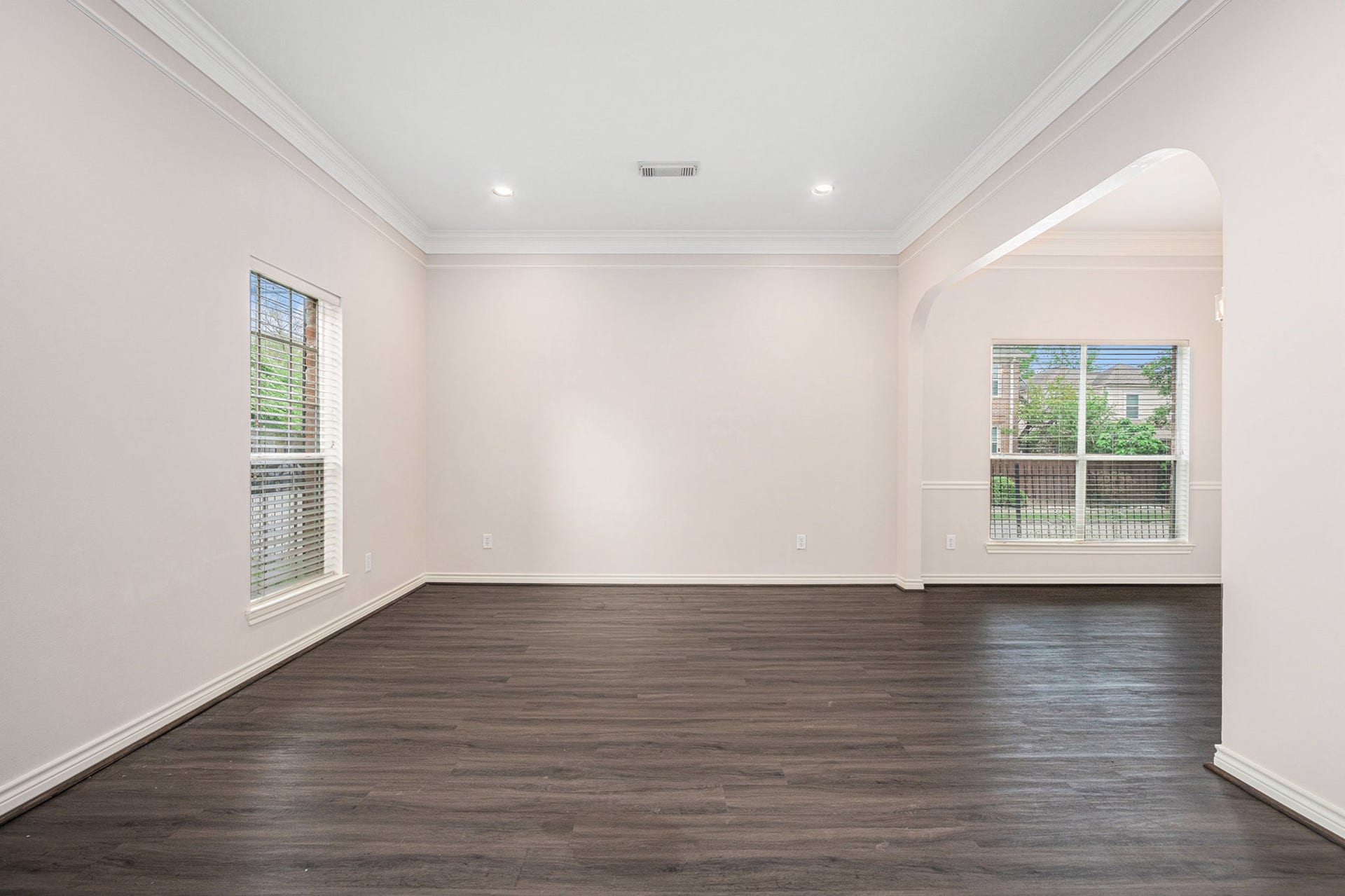 5001 Jackson Street, Houston, TX 77004 This photo showcases a bright, spacious room with light-colored walls and dark hardwood floors. It features large windows for natural light and an open layout with an arched entryway, perfect for versatile living and dining options.