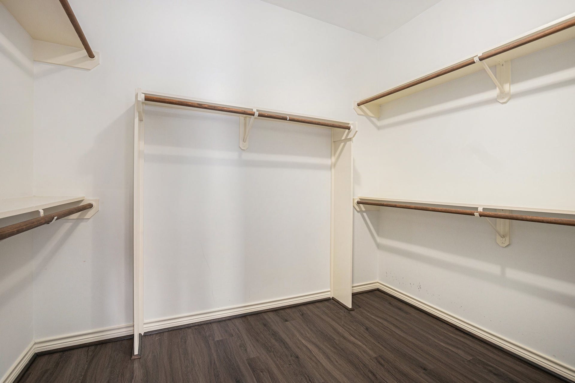 5001 Jackson Street, Houston, TX 77004 This photo shows a spacious walk-in closet with white walls, multiple wooden hanging rods, and dark wood flooring, offering ample storage space.