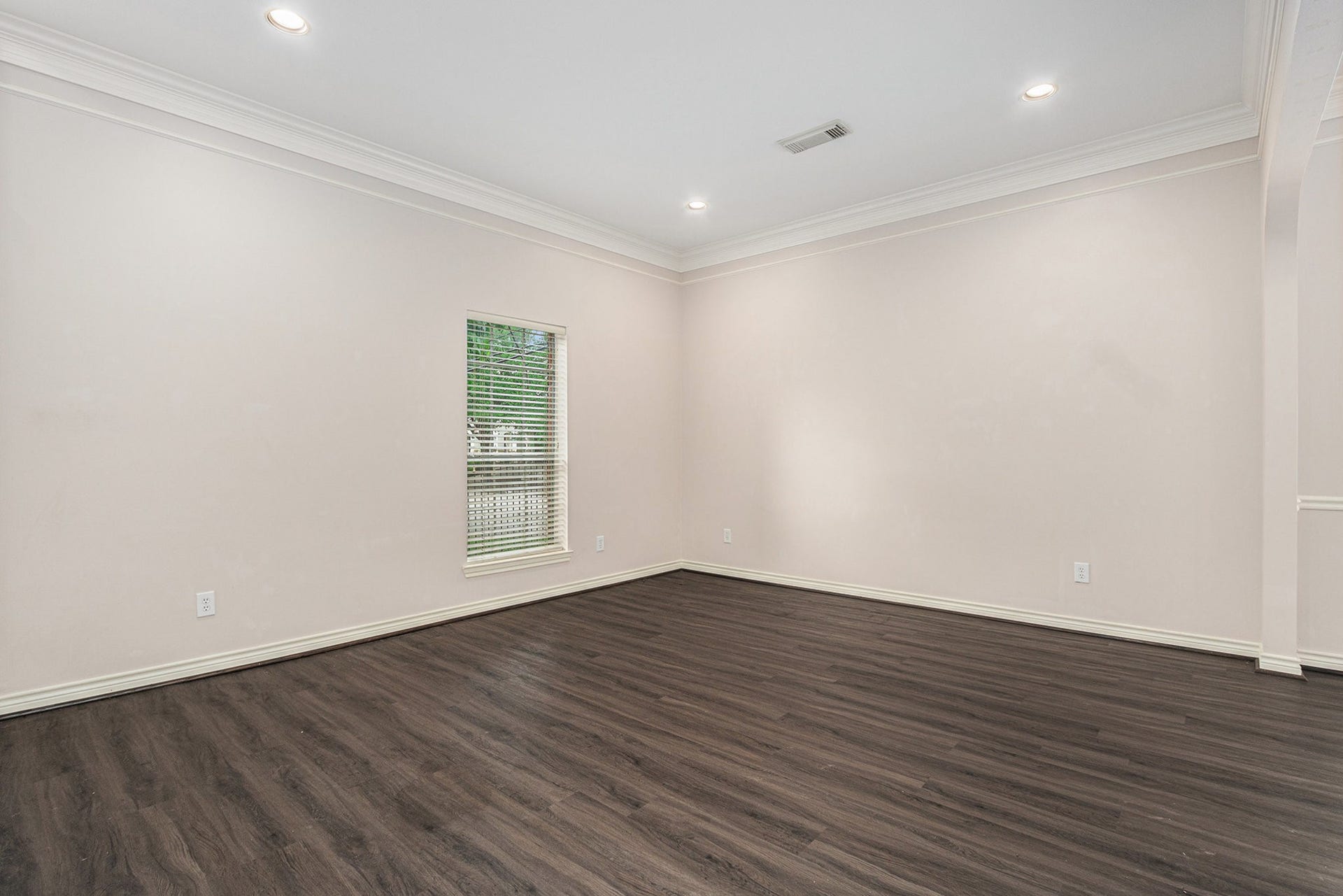 5001 Jackson Street, Houston, TX 77004 This spacious room features sleek dark wood flooring, neutral walls, and recessed lighting, creating a modern and inviting atmosphere. A large window brings in natural light, enhancing the room's bright and airy feel.