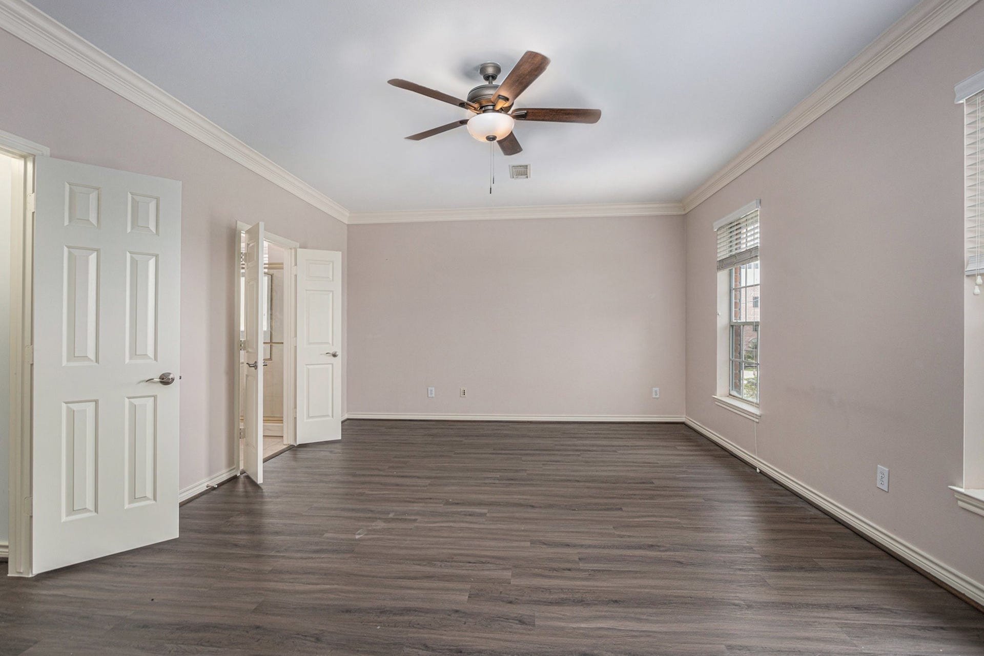 5001 Jackson Street, Houston, TX 77004 This spacious room features elegant crown molding, a ceiling fan, and rich wood flooring. It offers plenty of natural light through large windows, and has a neutral color palette, creating a welcoming atmosphere.