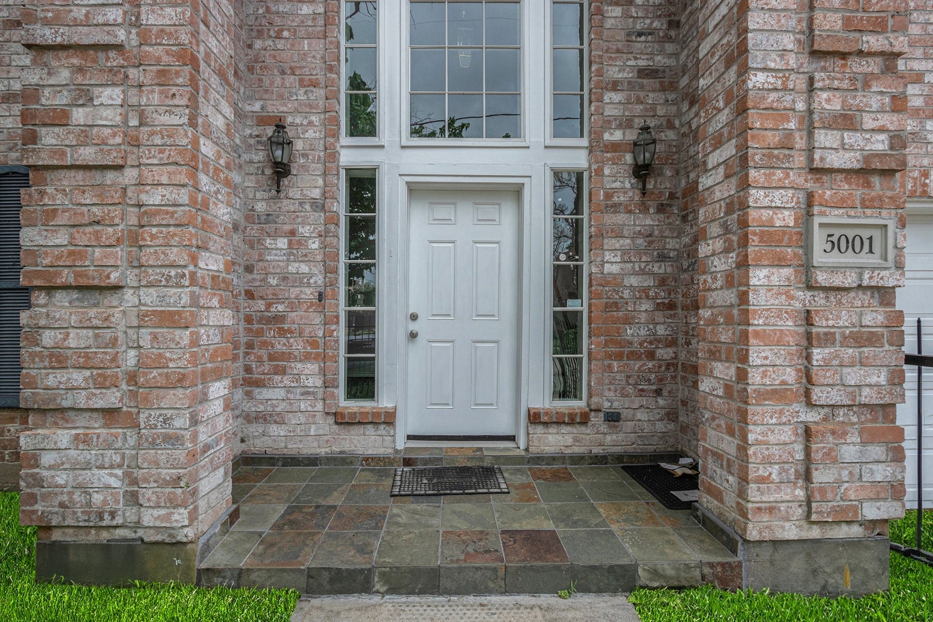 5001 Jackson Street, Houston, TX 77004 This entrance features a brick facade with a welcoming white door and large windows, allowing natural light into the home. The slate-tiled porch adds a touch of elegance, complemented by decorative outdoor lighting.