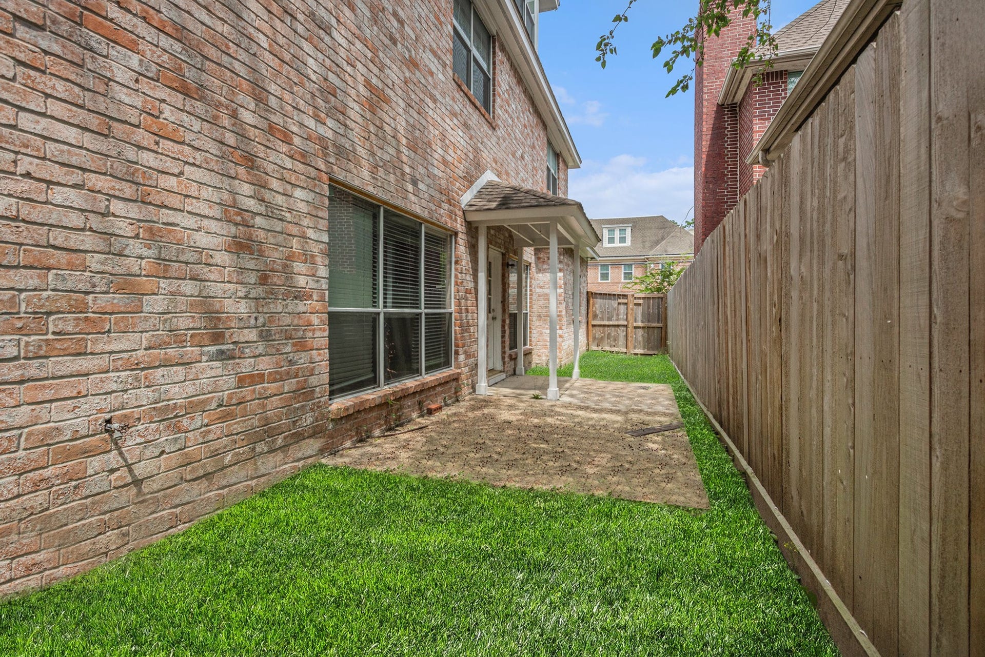 5001 Jackson Street, Houston, TX 77004 This photo shows a fenced backyard with a brick exterior, lush green grass, a small covered patio, and a wooden fence for privacy. Ideal for low-maintenance outdoor space.