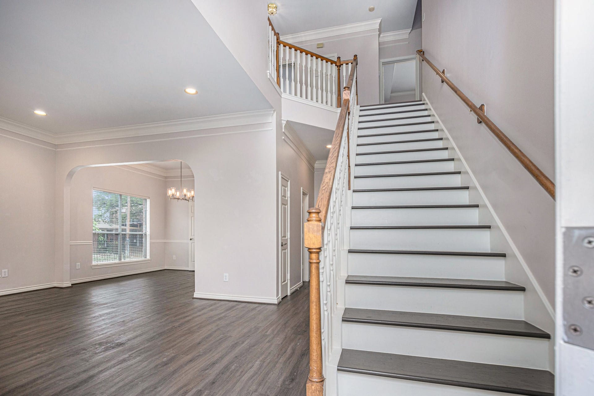 5001 Jackson Street, Houston, TX 77004 This photo showcases a bright, open entryway with elegant hardwood flooring, a staircase with wooden handrails, and a view into a spacious dining area featuring large windows and a modern chandelier.
