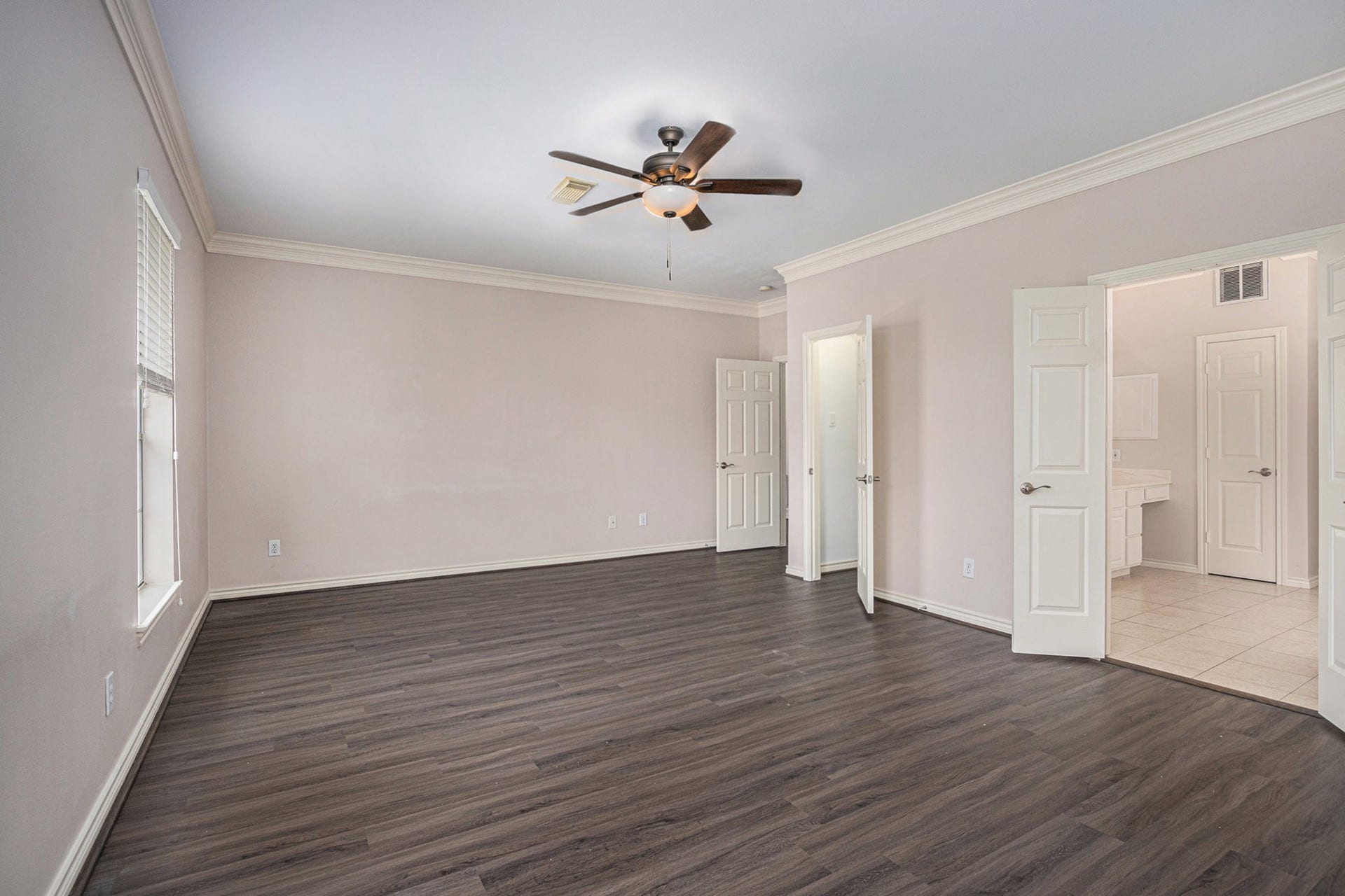 5001 Jackson Street, Houston, TX 77004 Spacious bedroom with dark wood flooring, neutral walls, and a ceiling fan. It features two doors leading to a bathroom and a closet, offering ample natural light through large windows.