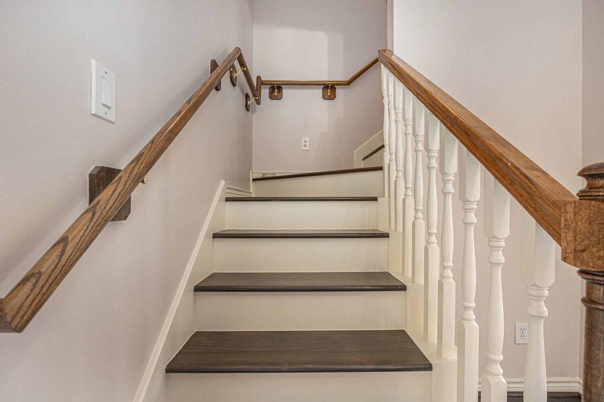 5001 Jackson Street, Houston, TX 77004 This photo showcases a staircase with dark wooden steps and white spindles, complemented by wooden handrails on both sides, leading to a landing. The walls are painted in a light, neutral color.