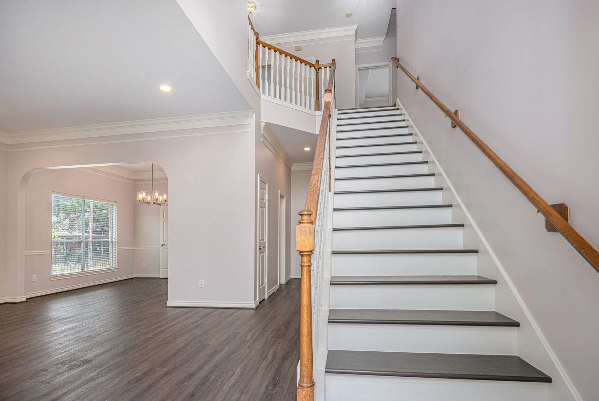 5001 Jackson Street, Houston, TX 77004 This photo showcases a bright, spacious entryway with elegant hardwood flooring, a prominent staircase with a wooden banister, and an open view into a dining area featuring a large window and chandelier.
