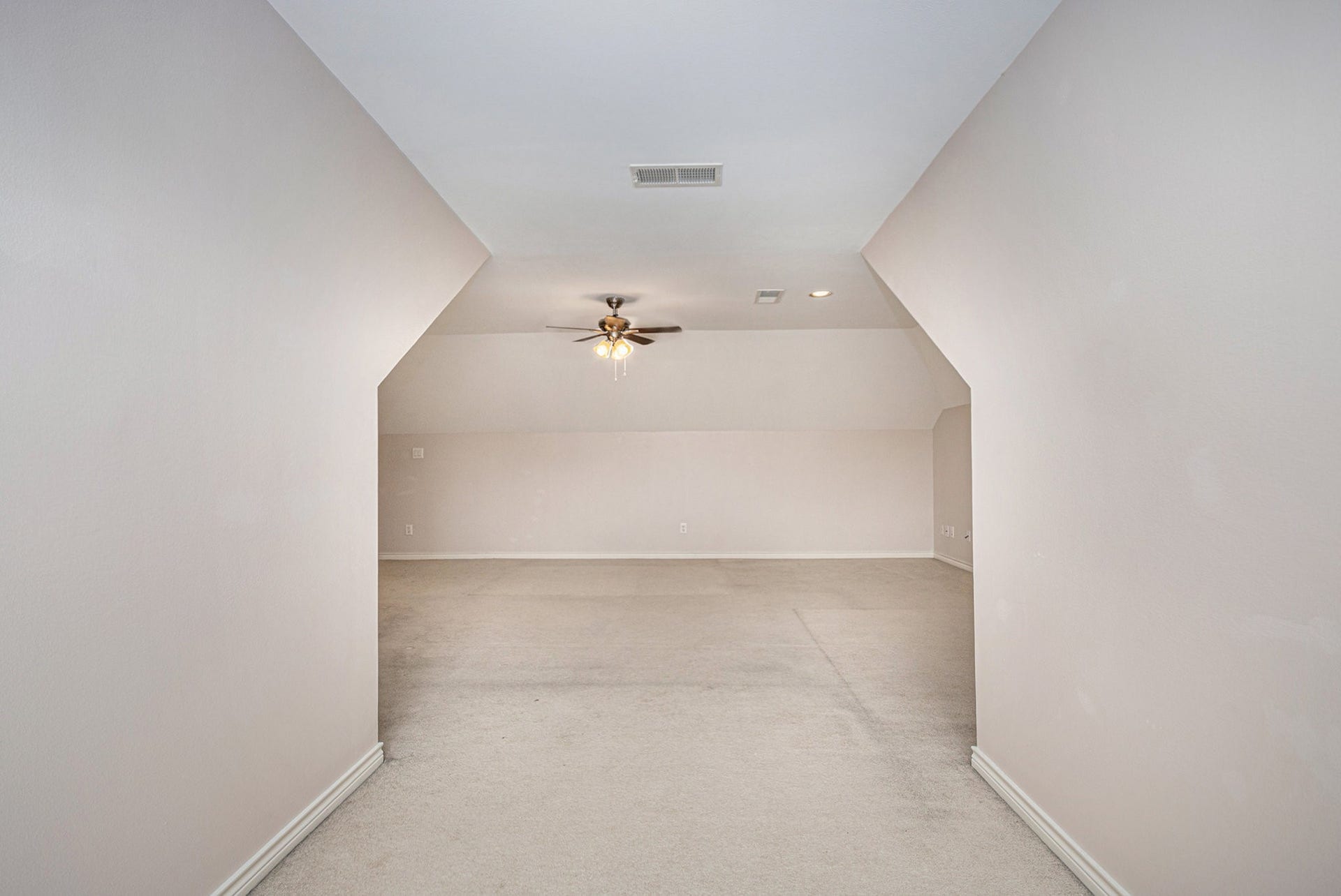 5001 Jackson Street, Houston, TX 77004 Spacious attic room with angled ceilings, neutral walls, and carpeted flooring, featuring a ceiling fan and recessed lighting. Ideal for a versatile living space or storage.