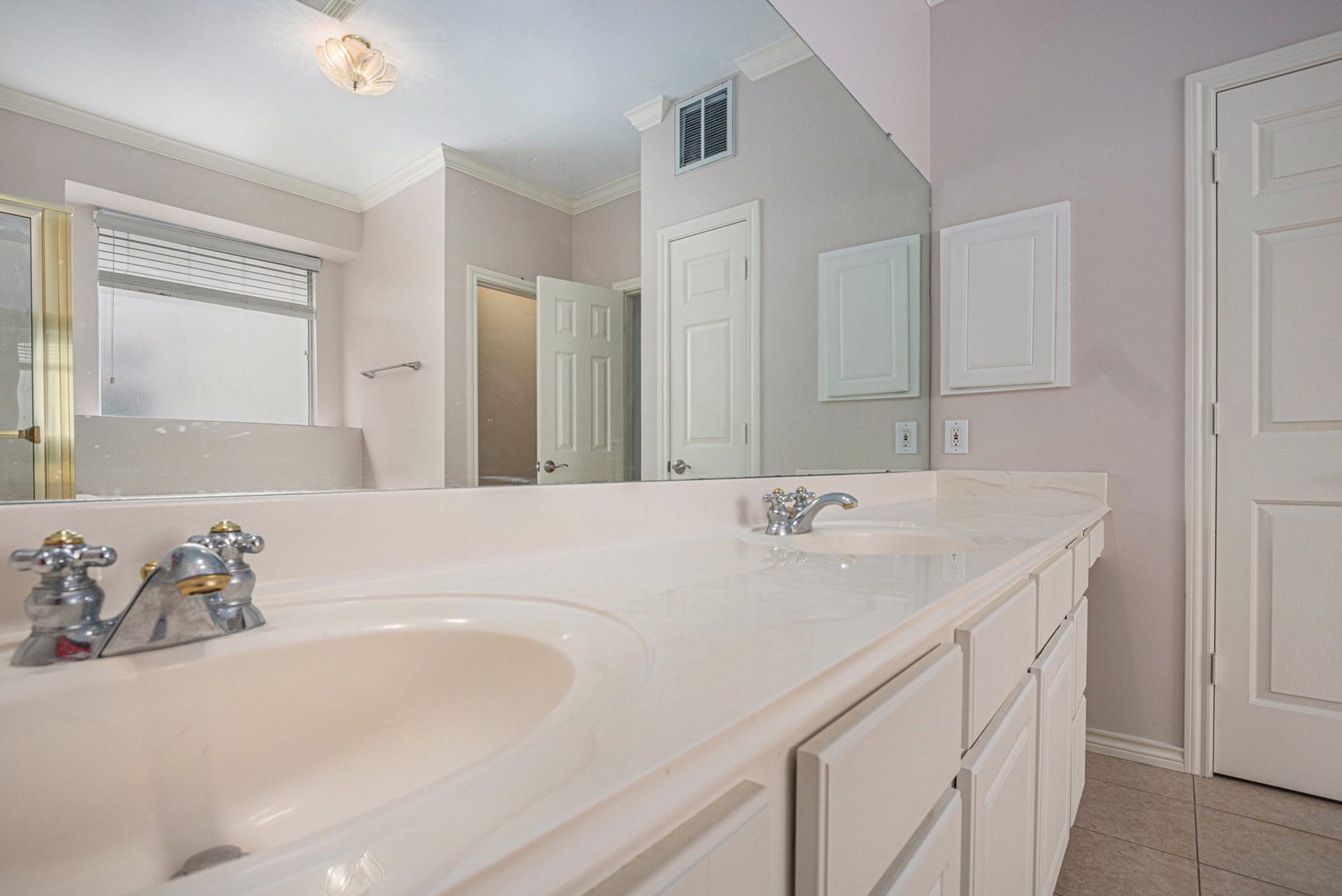 5001 Jackson Street, Houston, TX 77004 This bathroom features a spacious dual-sink vanity with ample counter space, a large mirror, and neutral tile flooring. The room is well-lit with natural light from a frosted window, offering privacy and elegance.