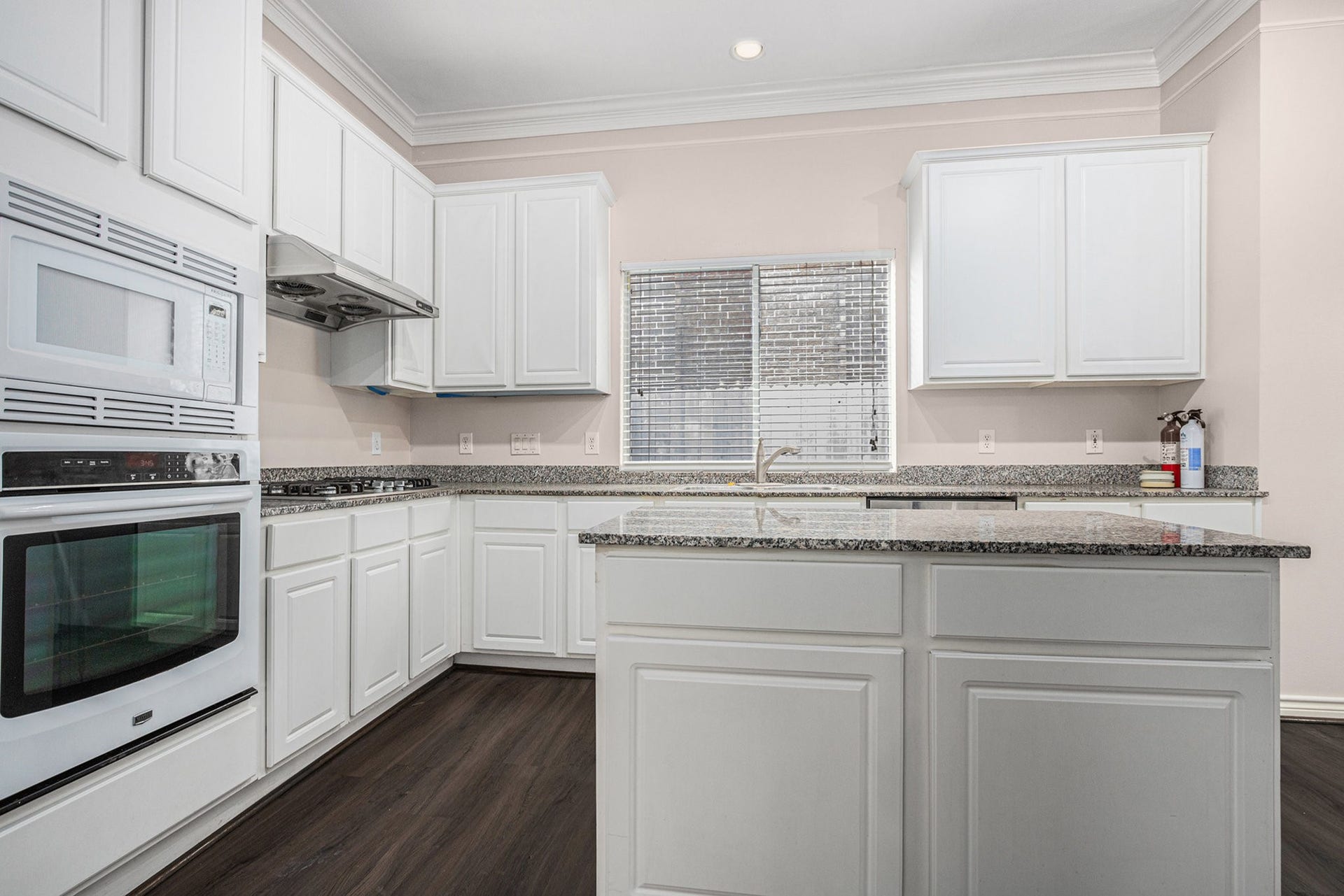 5001 Jackson Street, Houston, TX 77004 Bright and spacious kitchen with sleek white cabinetry, granite countertops, and modern appliances. The large window provides ample natural light, complementing the elegant dark wood flooring. Ideal for culinary enthusiasts.