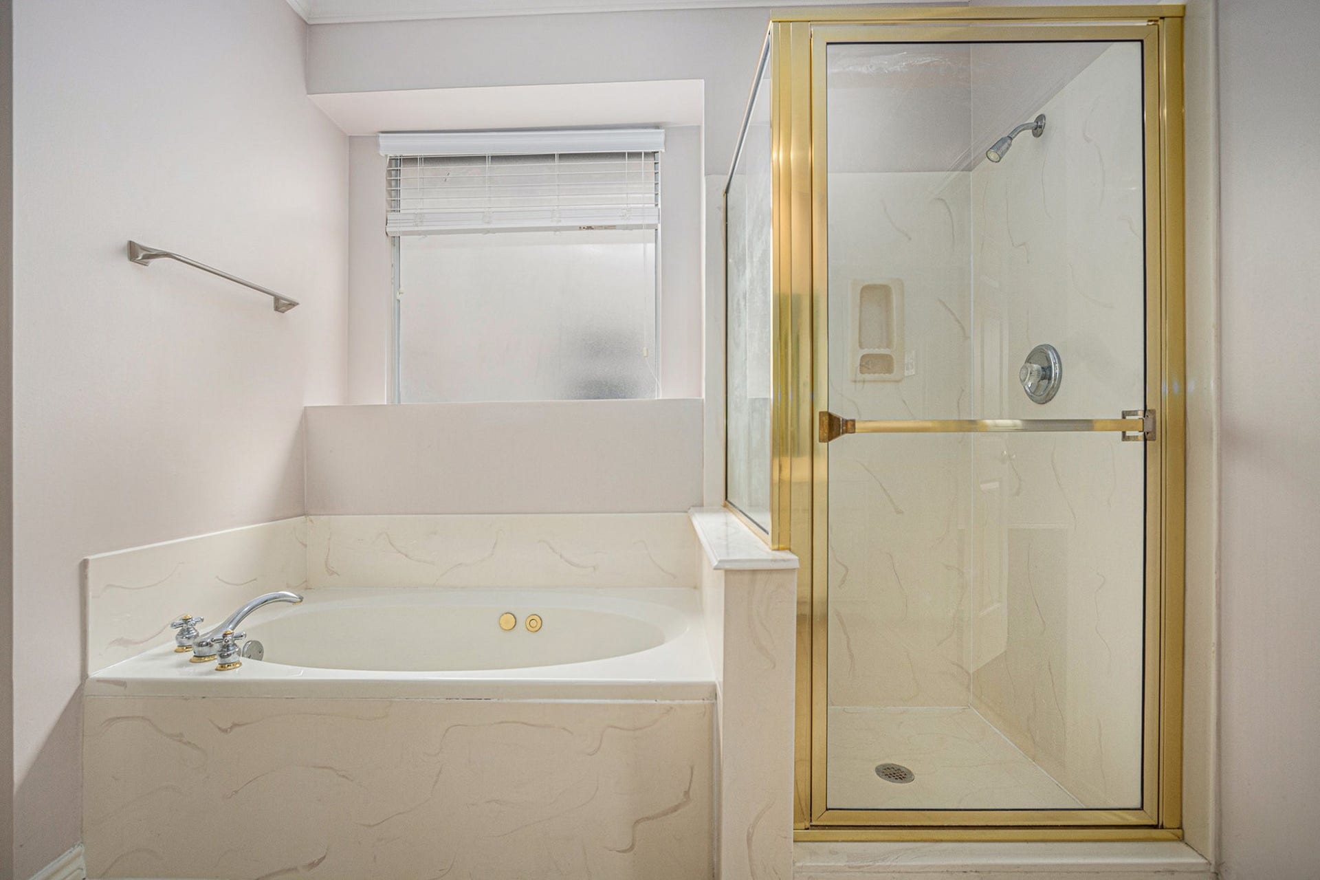 5001 Jackson Street, Houston, TX 77004 This bathroom features a spacious corner bathtub with sleek fixtures and a separate glass-enclosed shower, accented with gold trim. A frosted window provides natural light while maintaining privacy.
