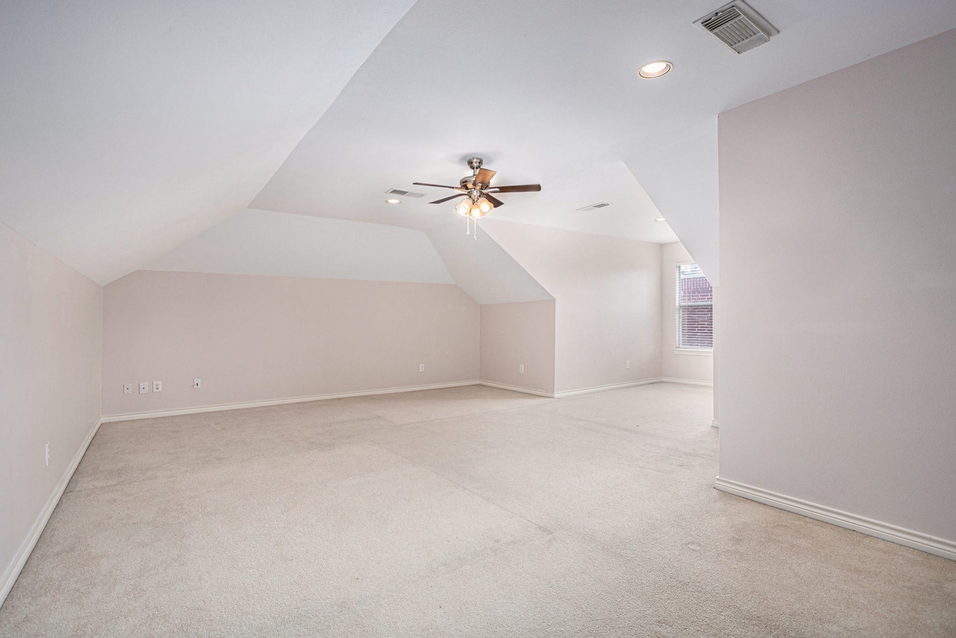 5001 Jackson Street, Houston, TX 77004 This spacious, light-filled room features a sloped ceiling and neutral carpet, perfect for a bedroom or home office. It includes a ceiling fan and a window for natural light.