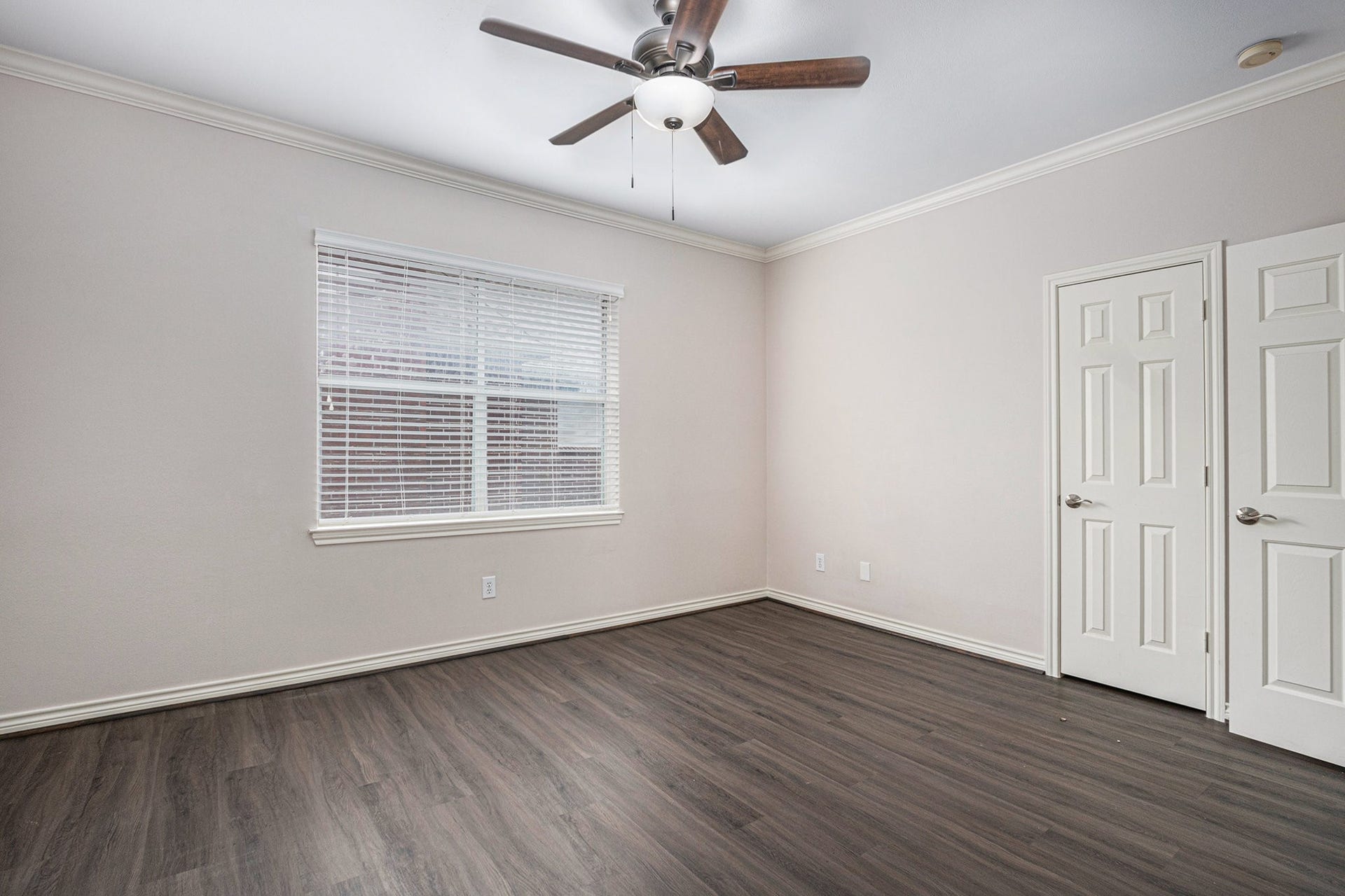 5001 Jackson Street, Houston, TX 77004 This room features laminate wood flooring, neutral walls, and a ceiling fan with light. A large window provides natural light, and there are two white doors, likely for closet space.
