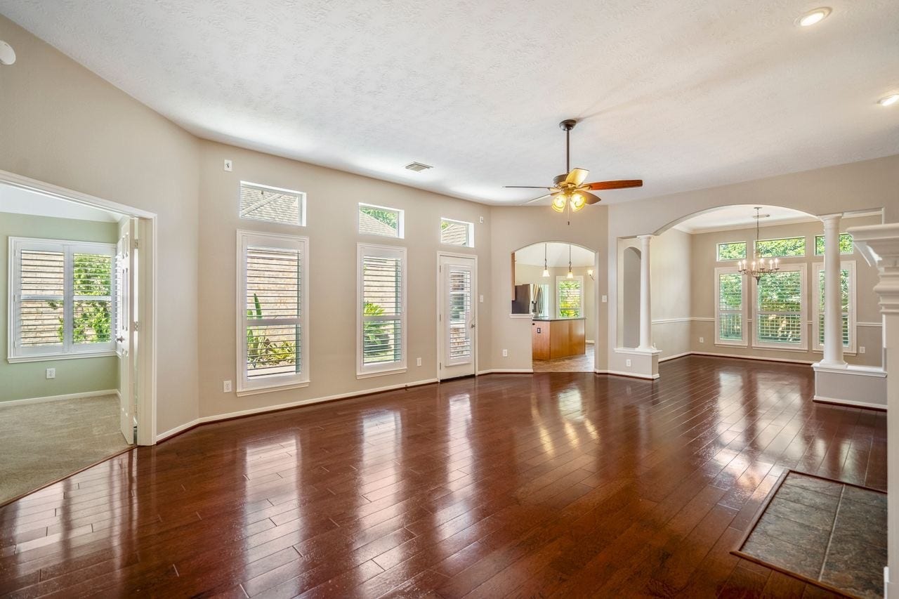 5210 Cottonwood Creek Lane, League City, TX 77573 Spacious open-concept living area with soaring ceilings, rich hardwood floors, abundant natural light, and seamless flow into the kitchen and formal dining space