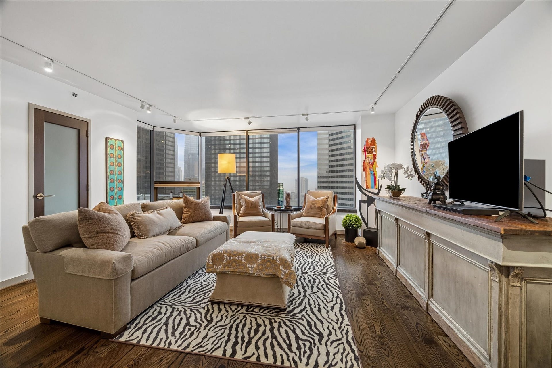1111 Caroline Street, #2601, Houston, TX 77010 Expansive windows frame downtown views across the living room. Automated Lutron shades provide convenient control over natural light, while wood floors and track lighting define the open space.